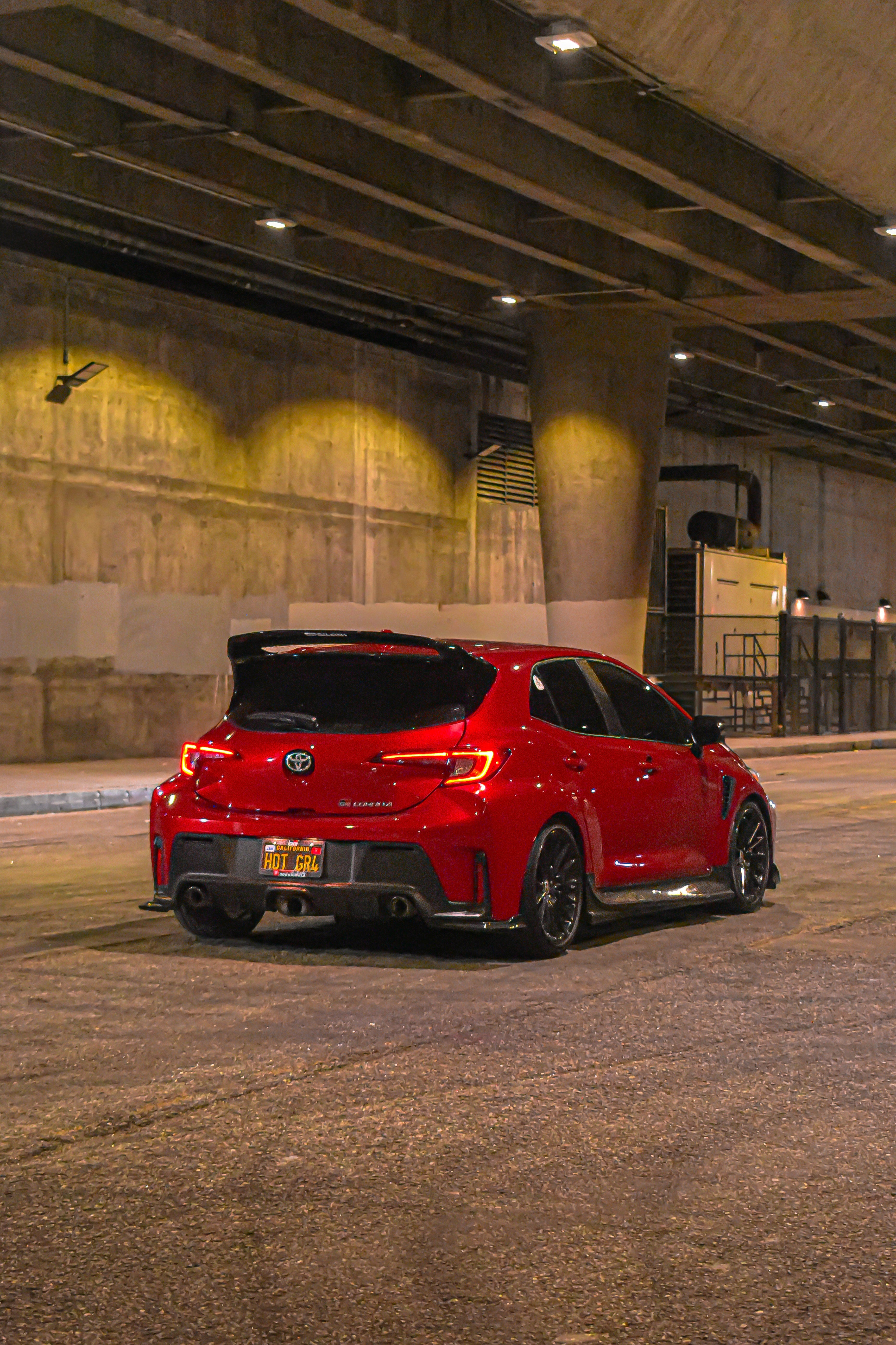 Rear three-quarter view of a red GR Corolla with rear spats V2 in a parking garage at night