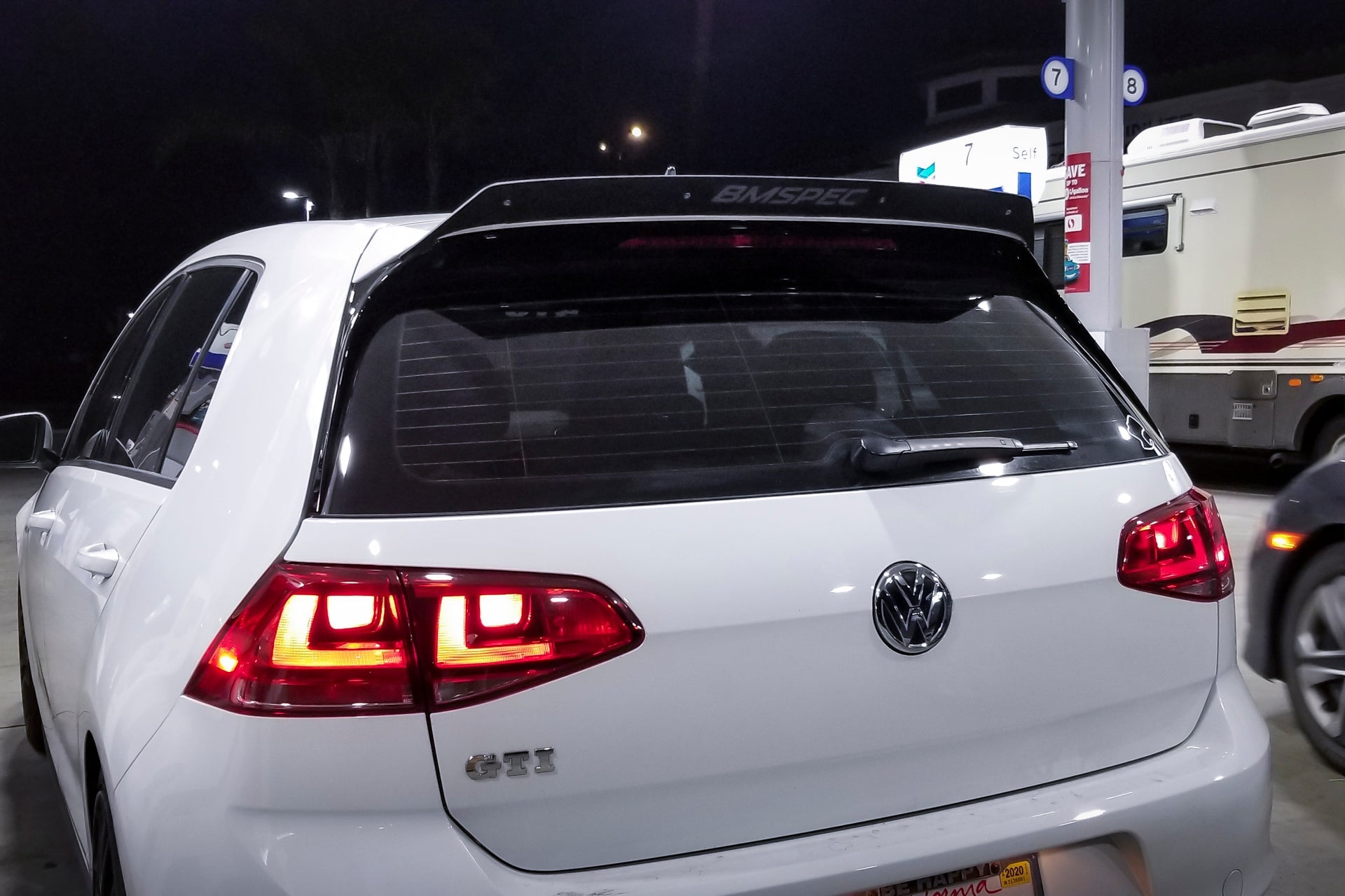 Rear view of a white Golf GTI with spoiler extension at a gas station at night