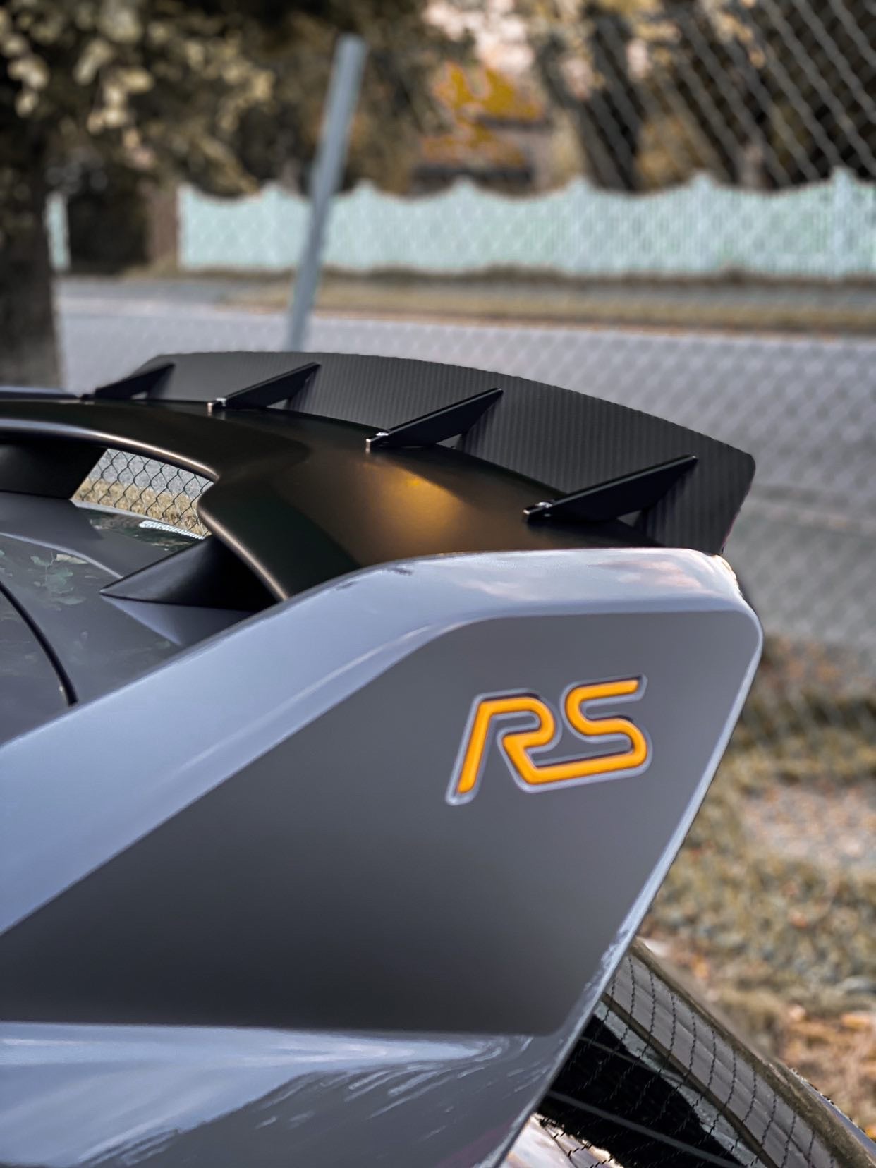 Carbon fiber spoiler extension close-up on a gray Focus RS with RS badge visible