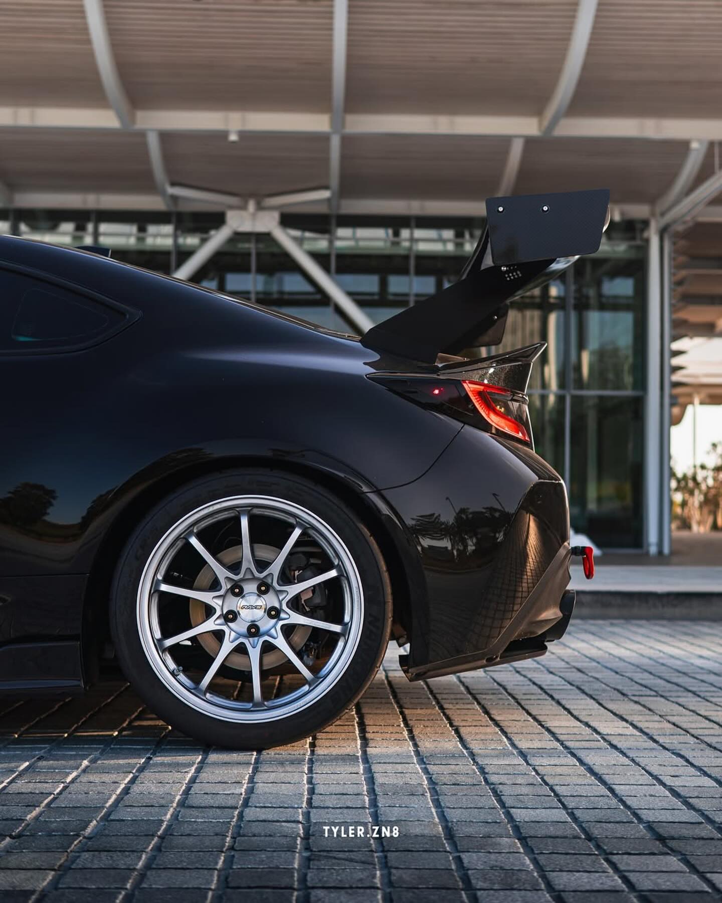 Rear three-quarter view of a black BRZ ZN8 with GT wing near flowers