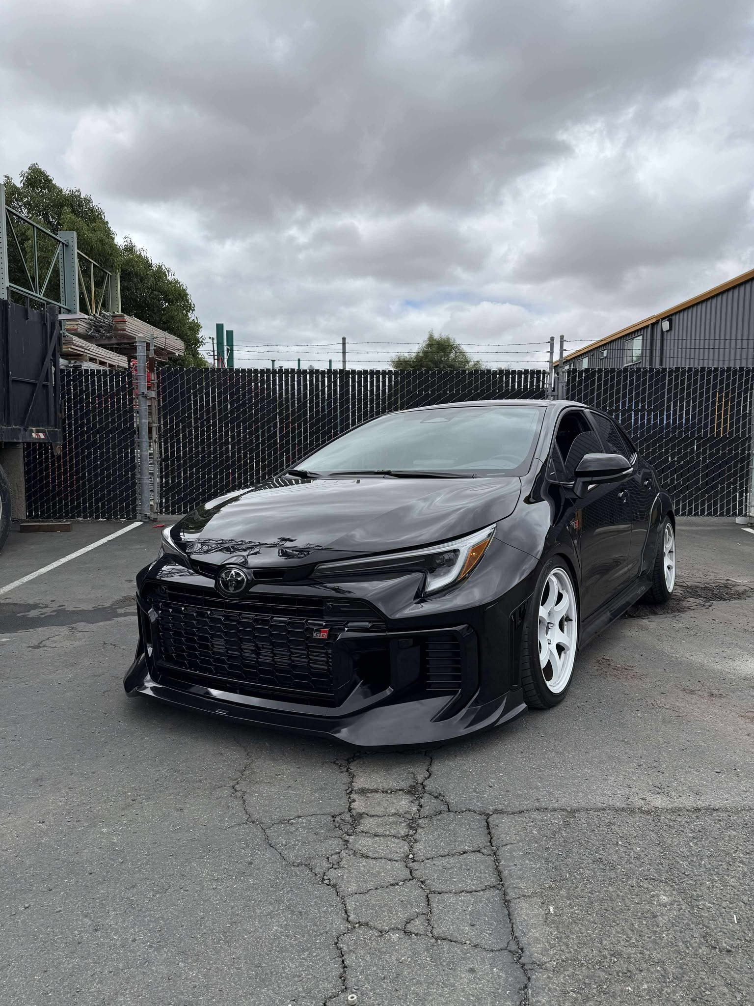 Front three-quarter view of a black GR Corolla Kouki with front lip under a cloudy sky