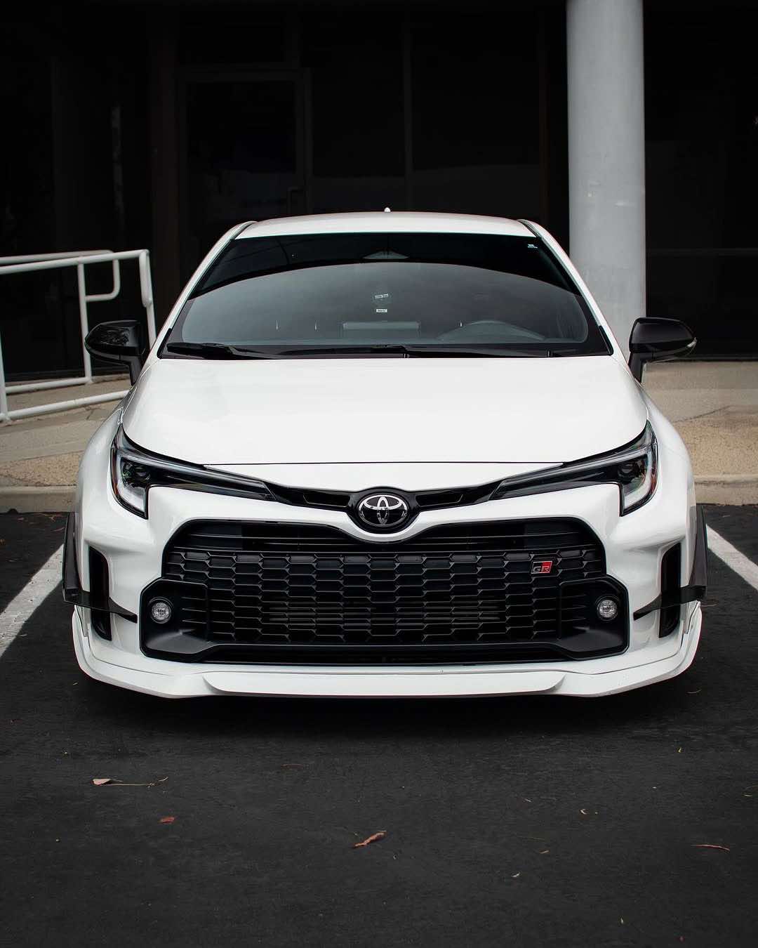 Front three-quarter view of a white GR Corolla with front lip parked on a hillside road