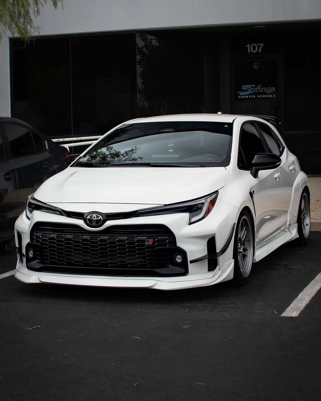 Front three-quarter view of a white GR Corolla with front lip in a parking lot
