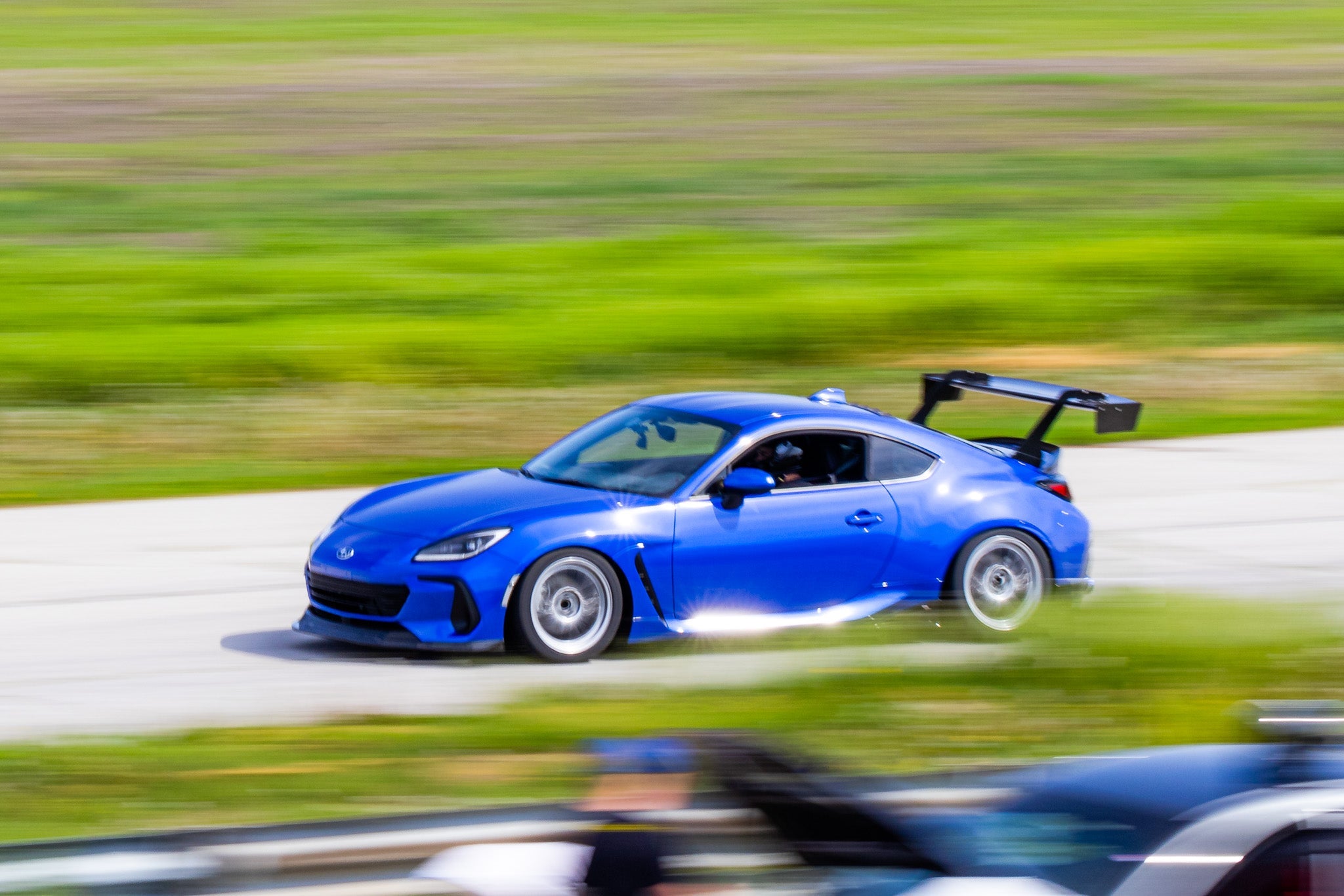 Side profile of a black BRZ ZN8 with GT wing near colorful flowerbeds