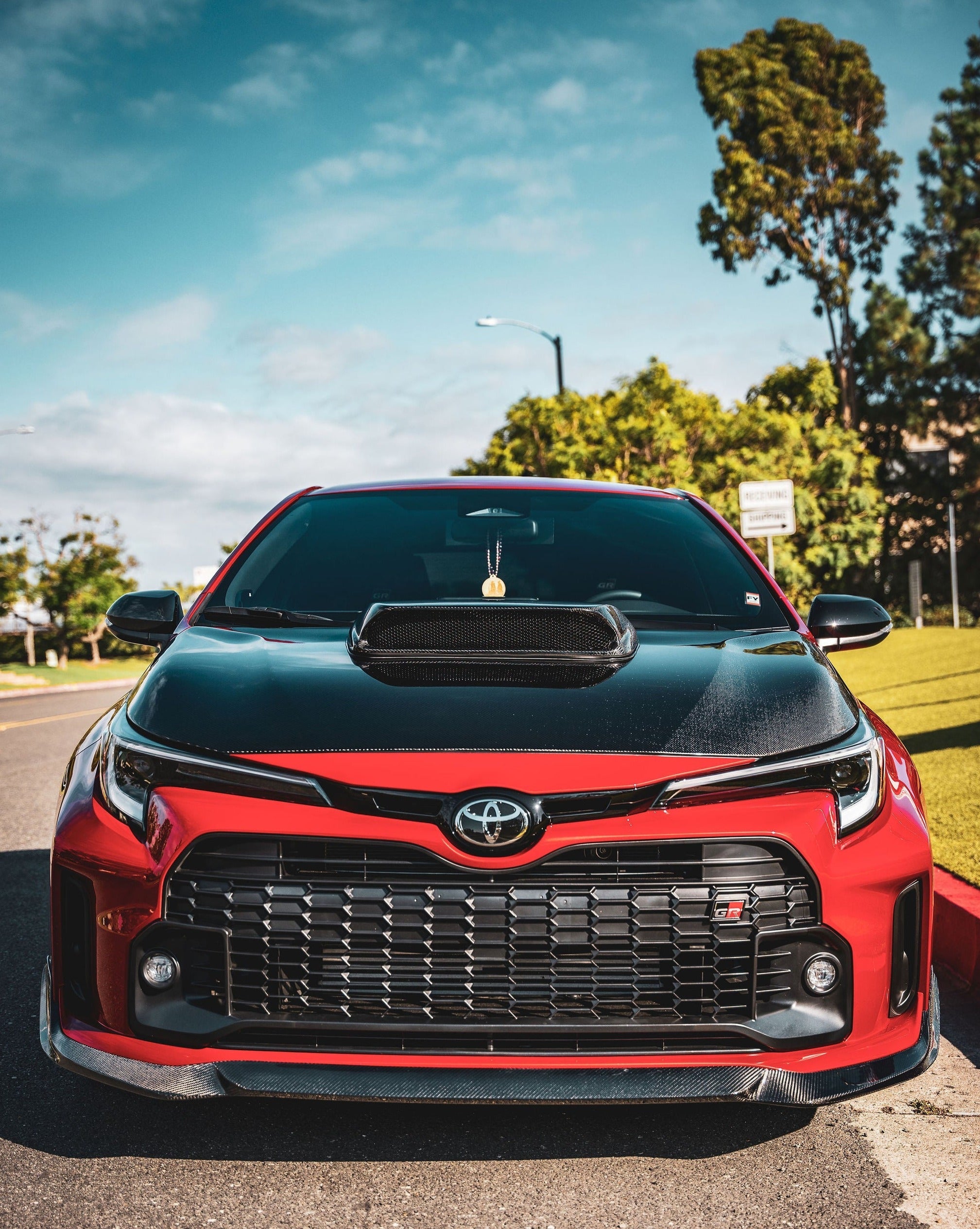Front three-quarter view of a red GR Corolla with front lip near flags outside a building