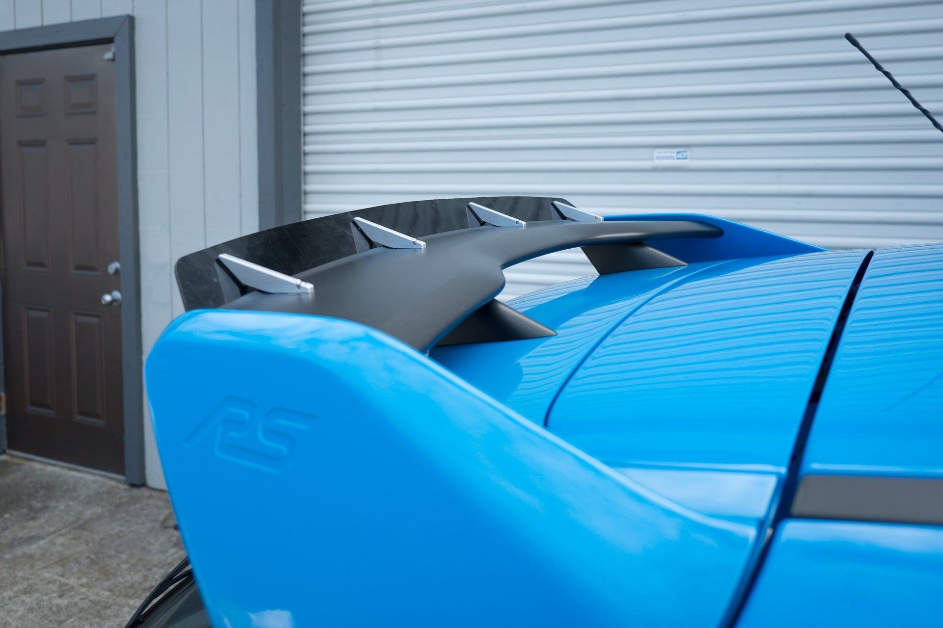Spoiler extension on a blue Focus RS parked next to a garage door