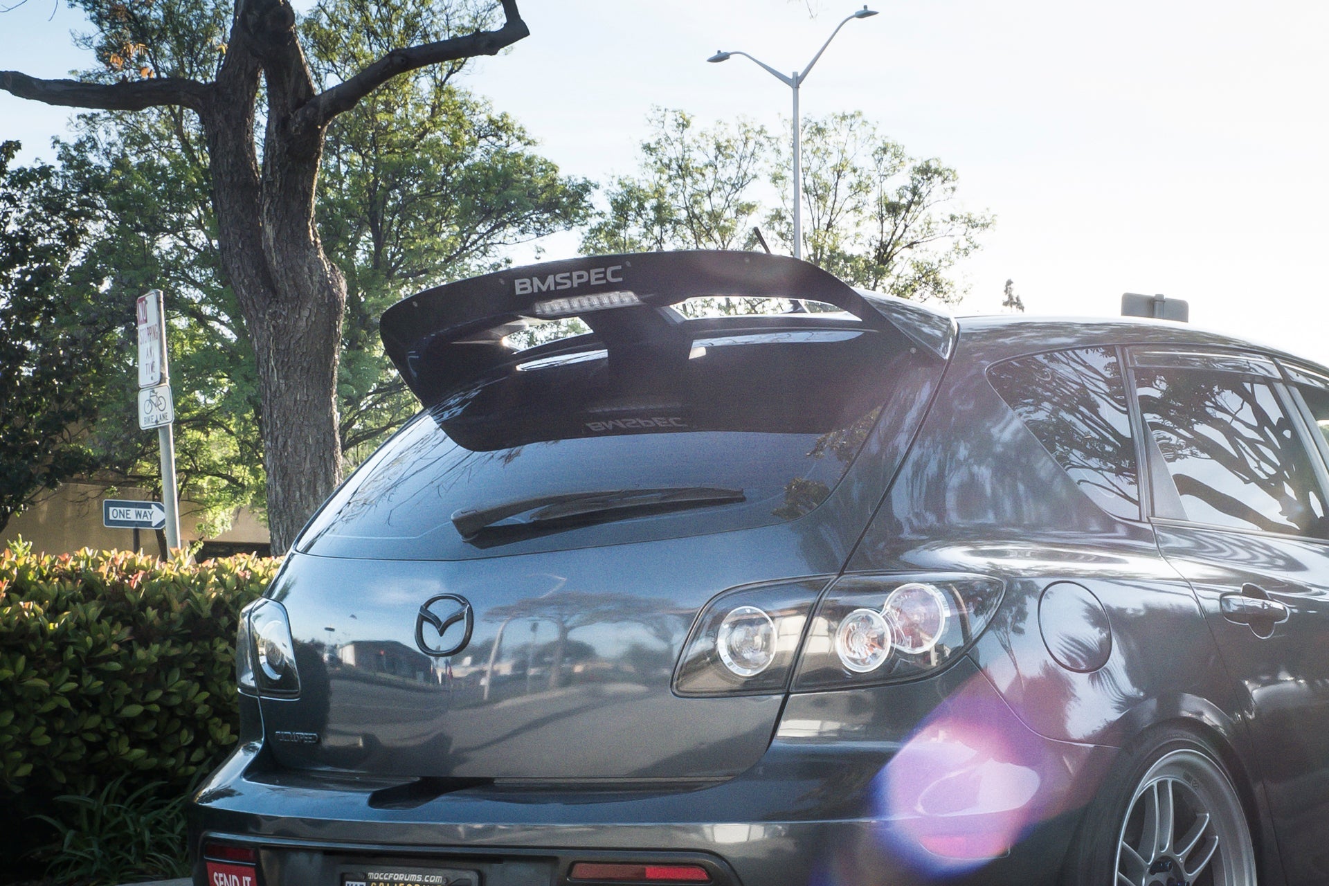 Rear three-quarter view of a gray Mazdaspeed3 Gen1 with Epsilon+ spoiler extension