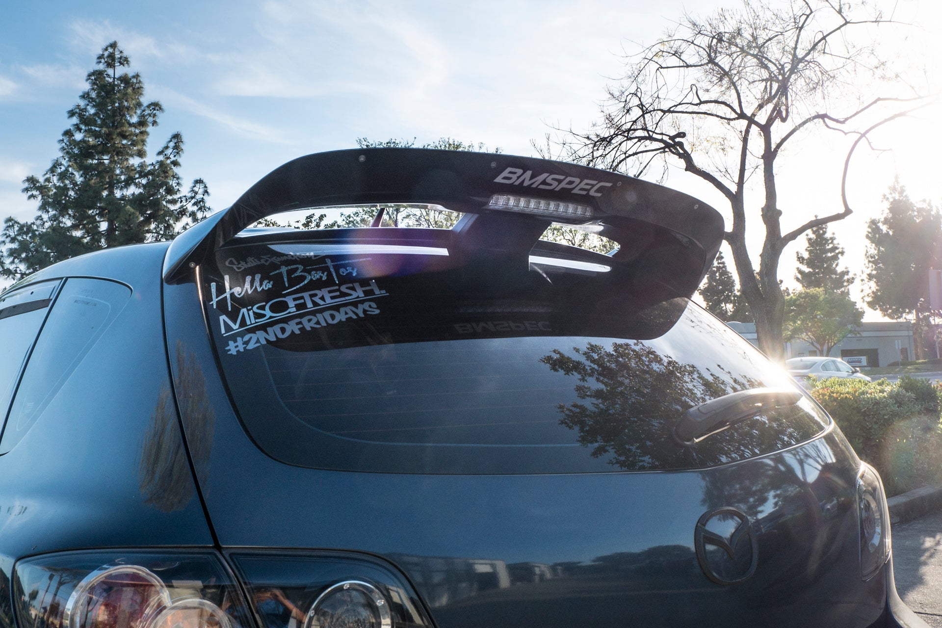 Rear view of a blue Mazdaspeed3 Gen1 with spoiler extension and window decals