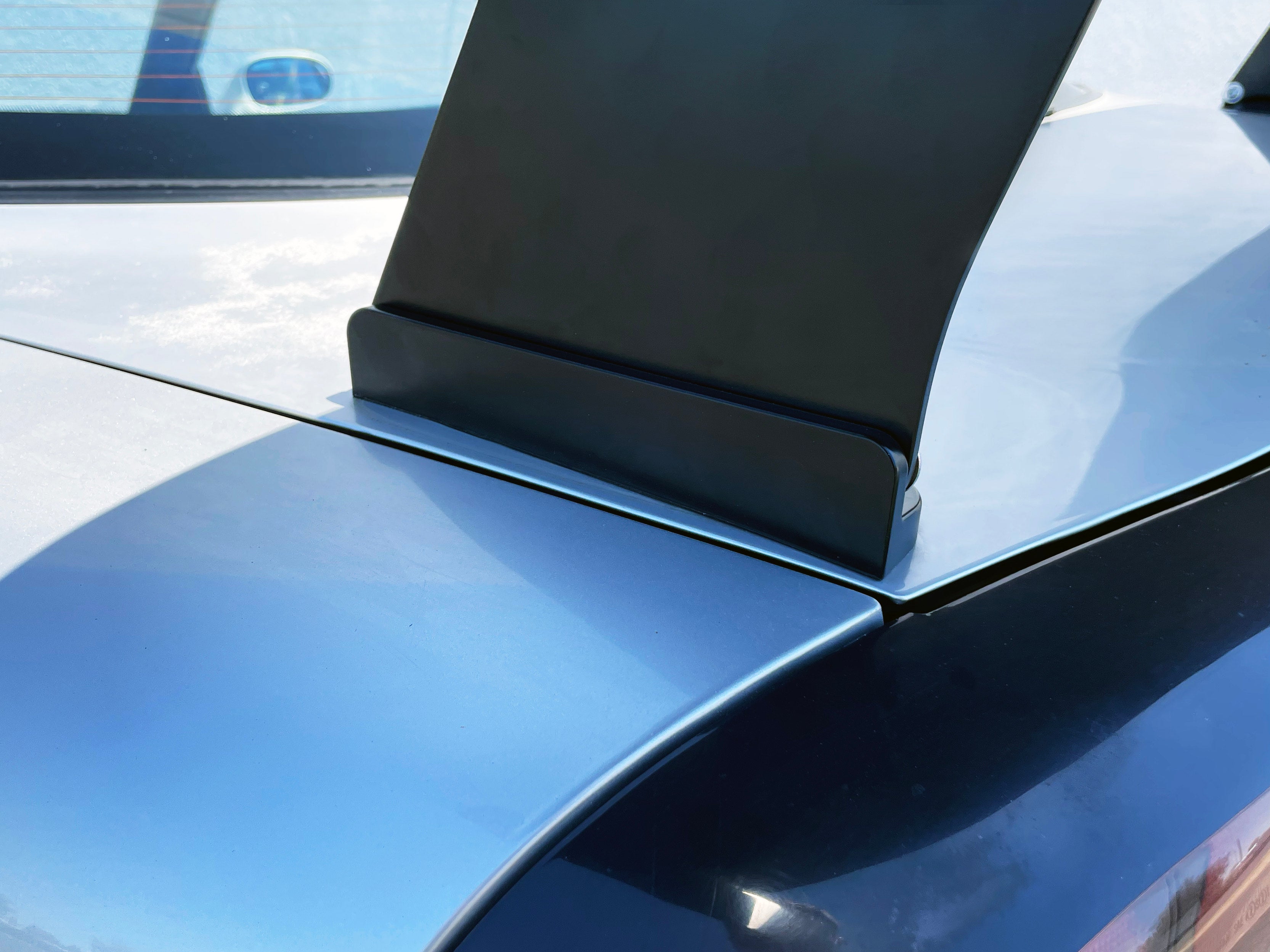 Close-up of the GT wing base mount on a blue RX-7 trunk lid