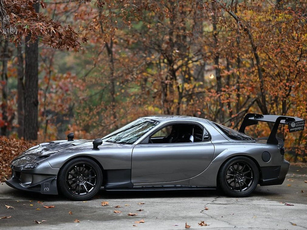 Side profile of a silver Mazda RX-7 FD with GT wing on an autumn road