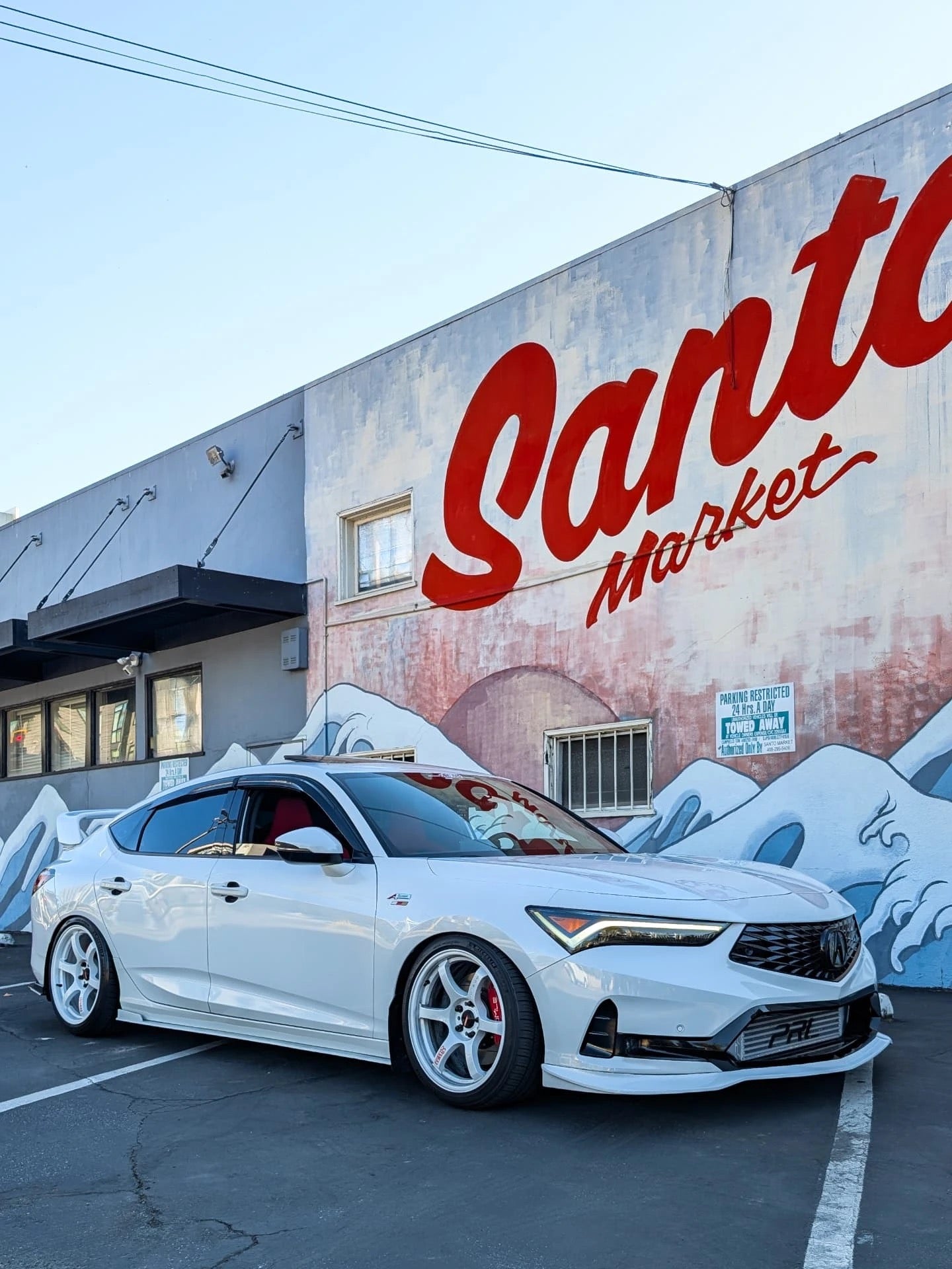 White Acura Integra with front lip parked beside a painted market mural