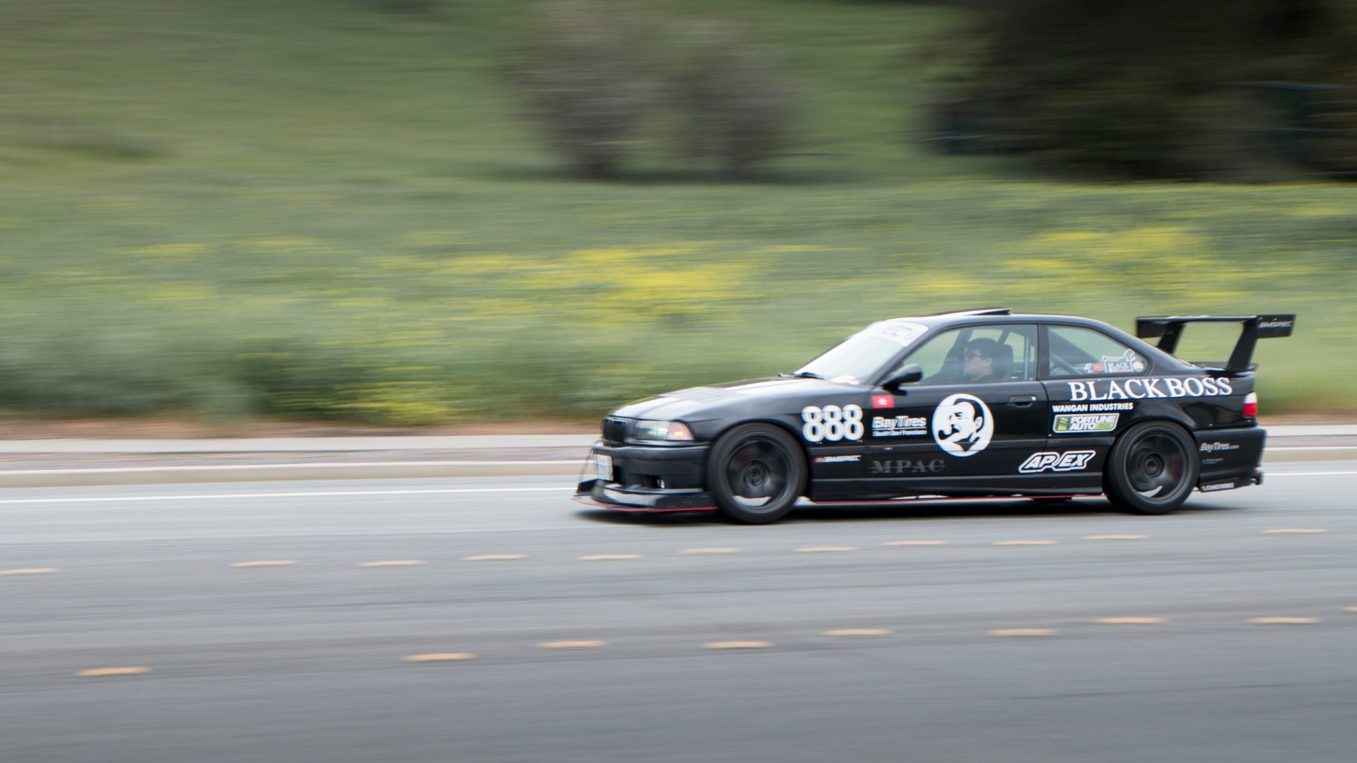 Black BMW E36 M3 race car with GT wing panning shot on a track