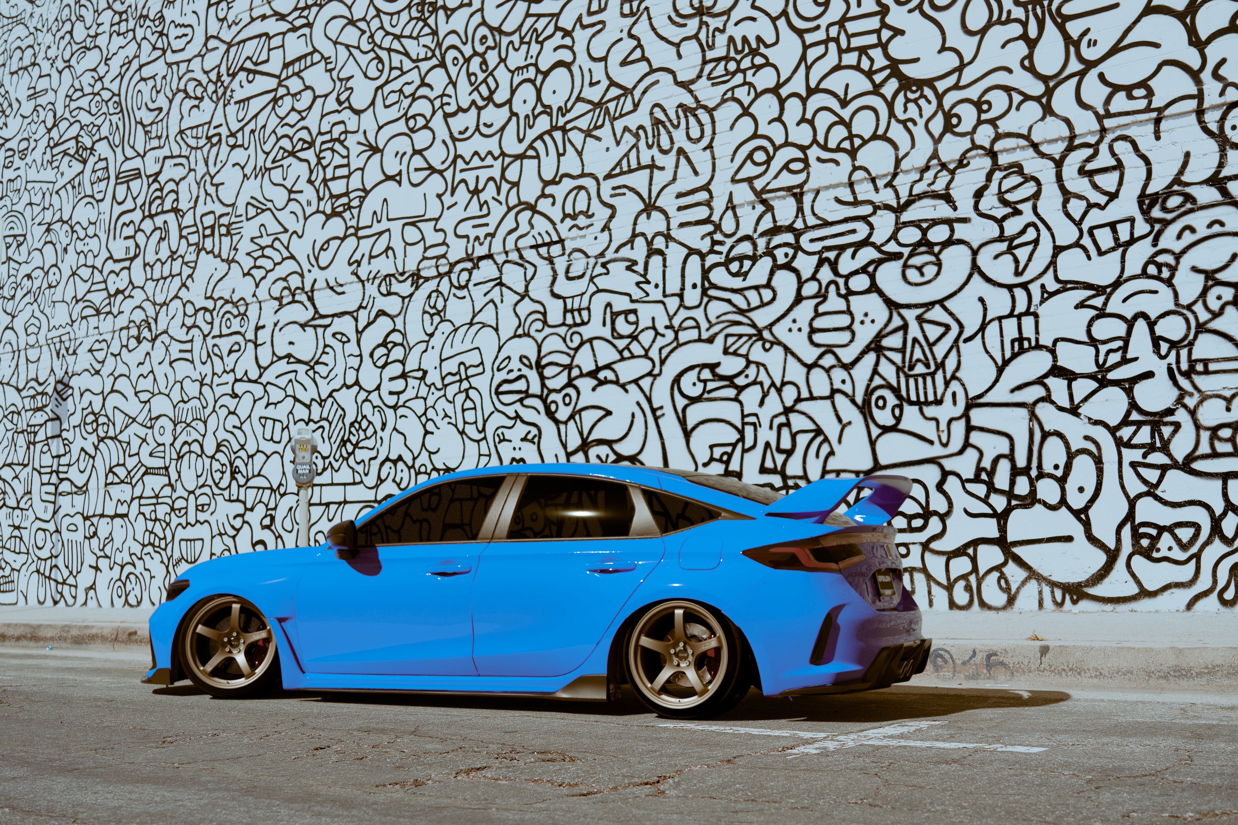 Rear three-quarter view of a blue Honda Civic FL5 with Sport Wing at a mural wall