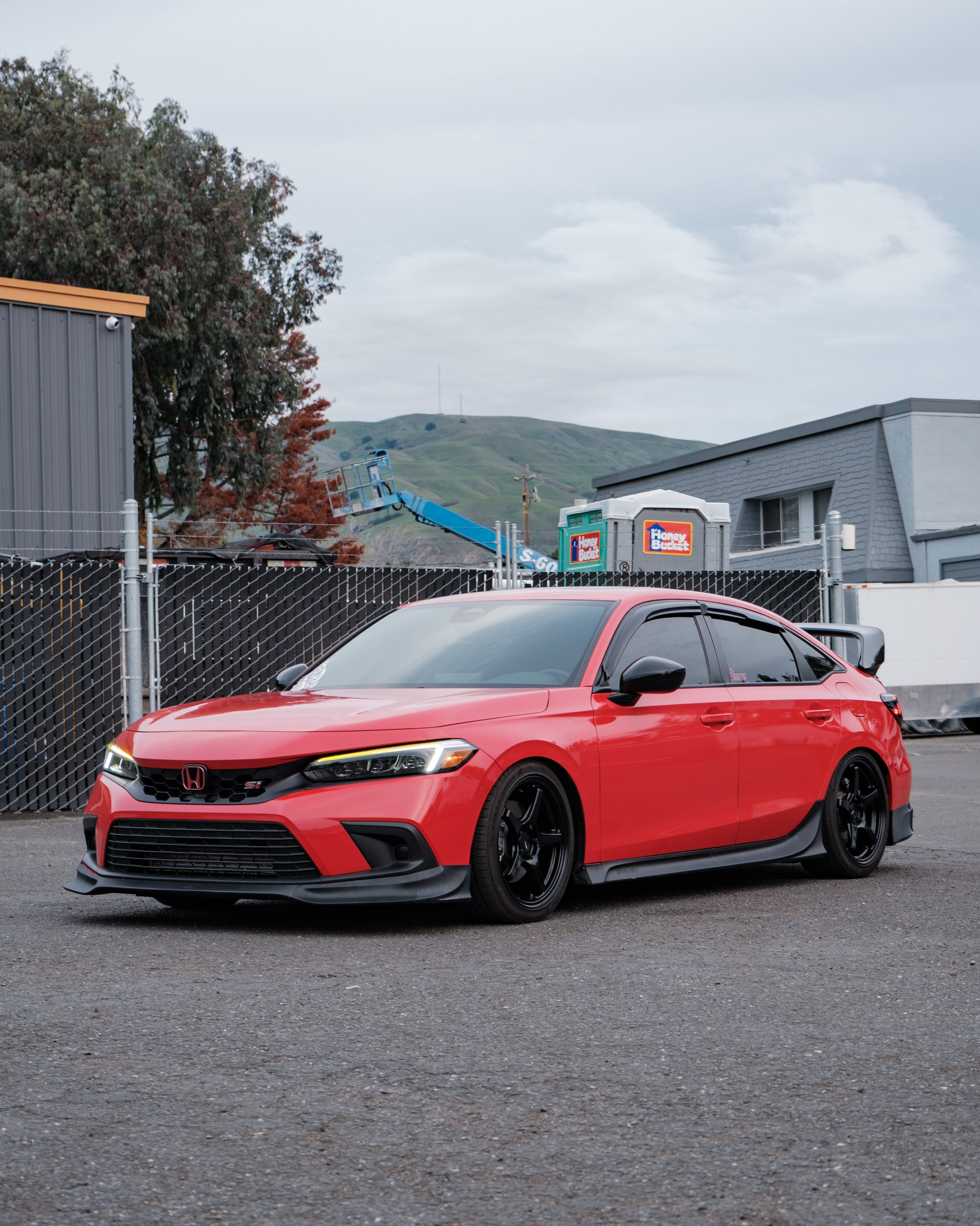 Red Honda Civic with front lip parked beside a chain-link fence