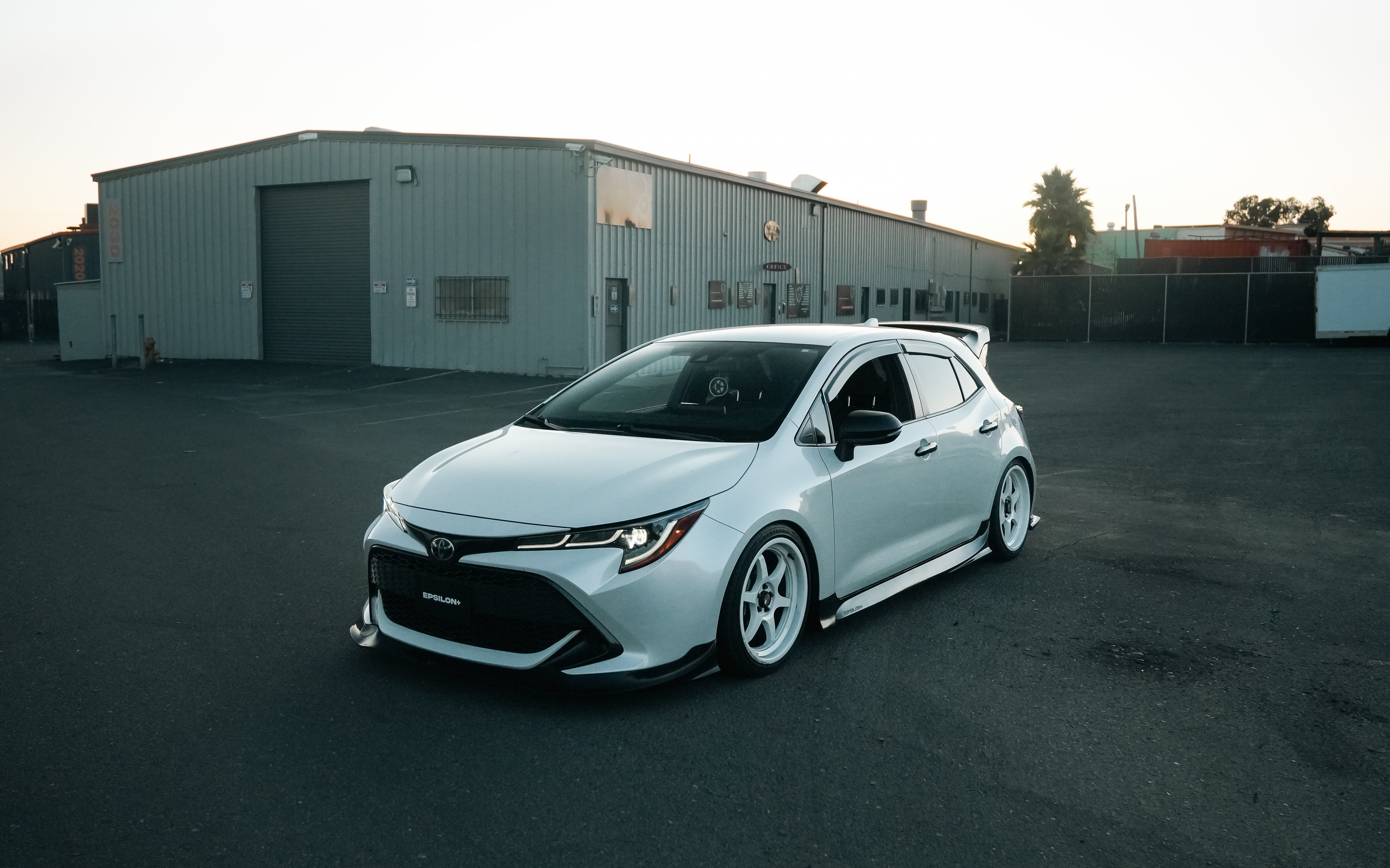 White Corolla Hatchback with side skirts parked beside a warehouse