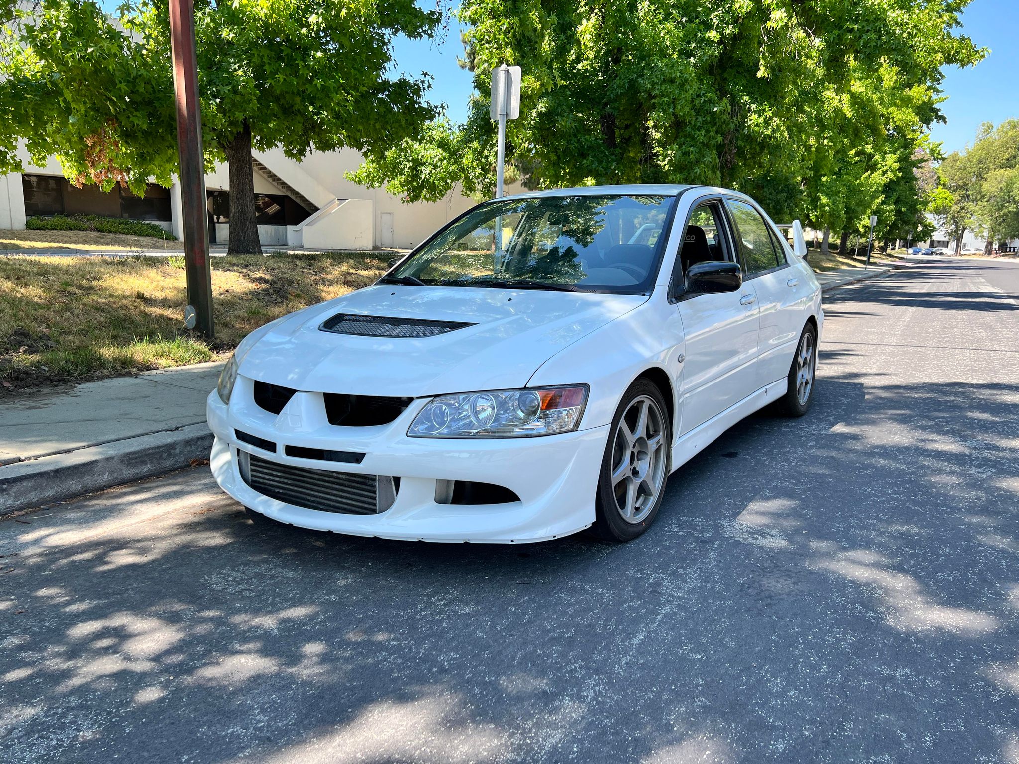 White Mitsubishi Evo 8 with front bumper parked on a tree-lined street