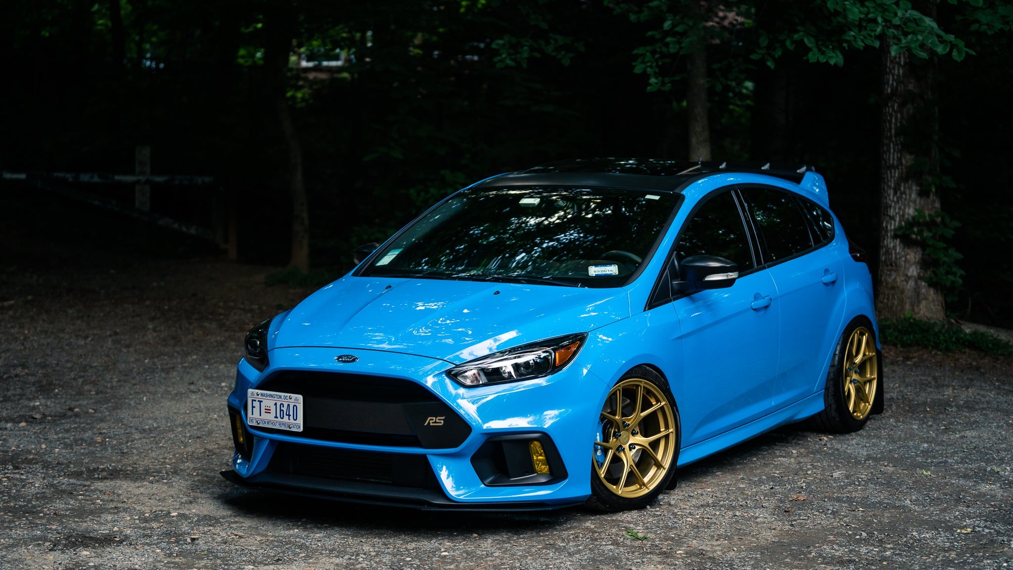 Blue Focus RS with front lip and gold wheels parked on a gravel road