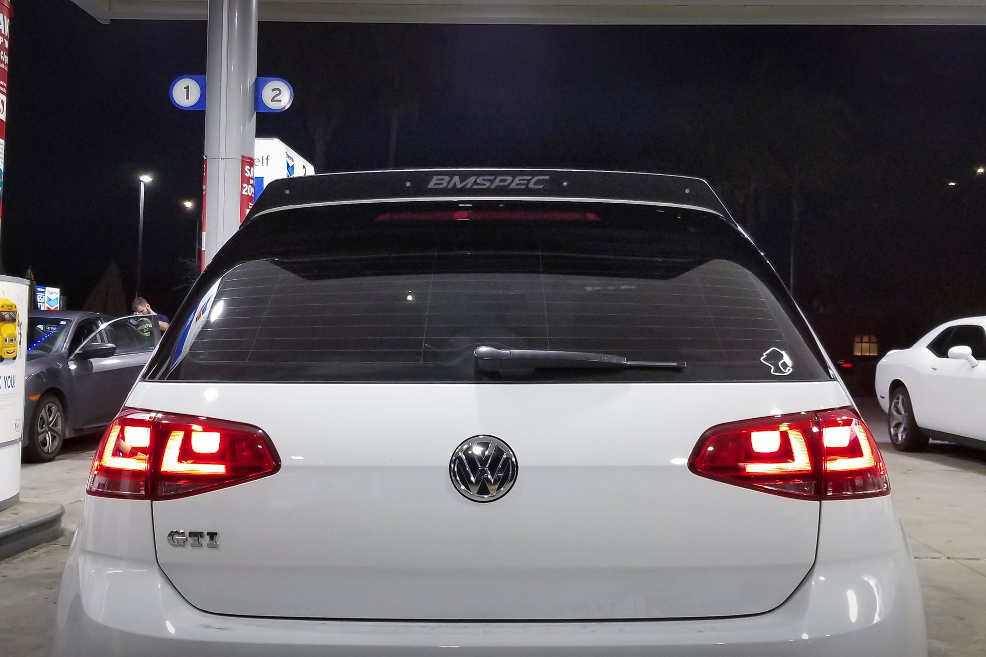 Rear close-up of a white Golf GTI with spoiler extension, taillights lit
