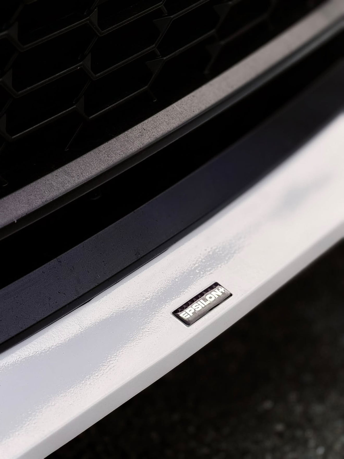 Close-up of the Epsilon+ badge on the painted white front lip of a GR Corolla Kouki