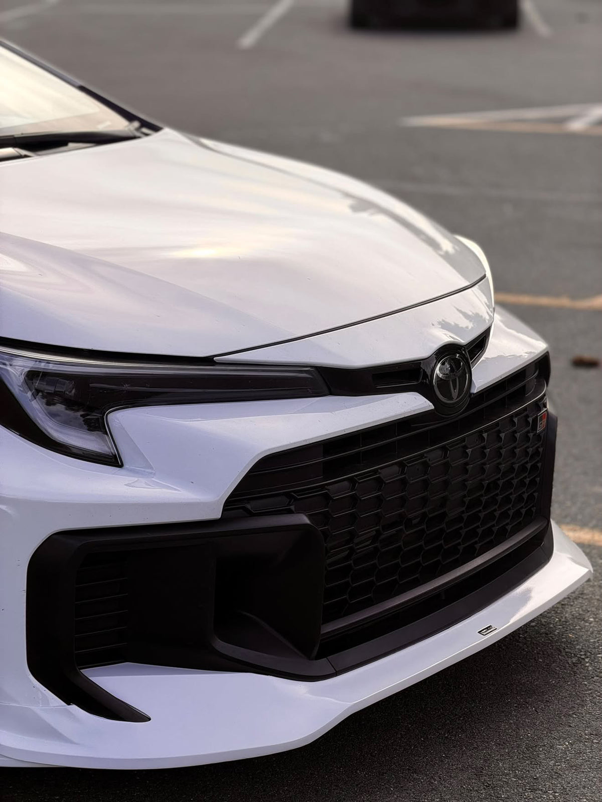Front three-quarter close-up of a white GR Corolla Kouki with front lip in a parking lot