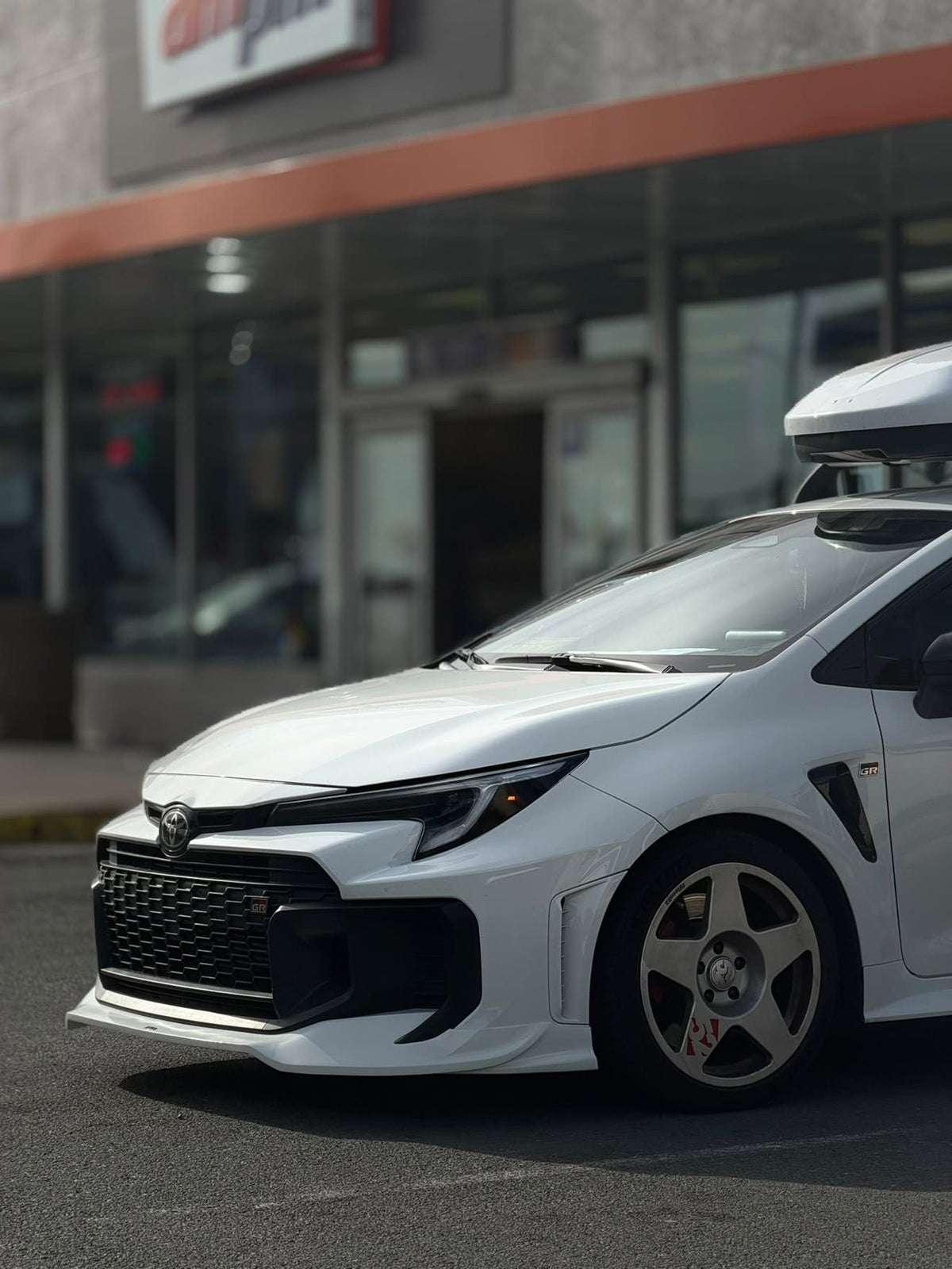 Front three-quarter view of a white GR Corolla Kouki with front lip parked outside a storefront