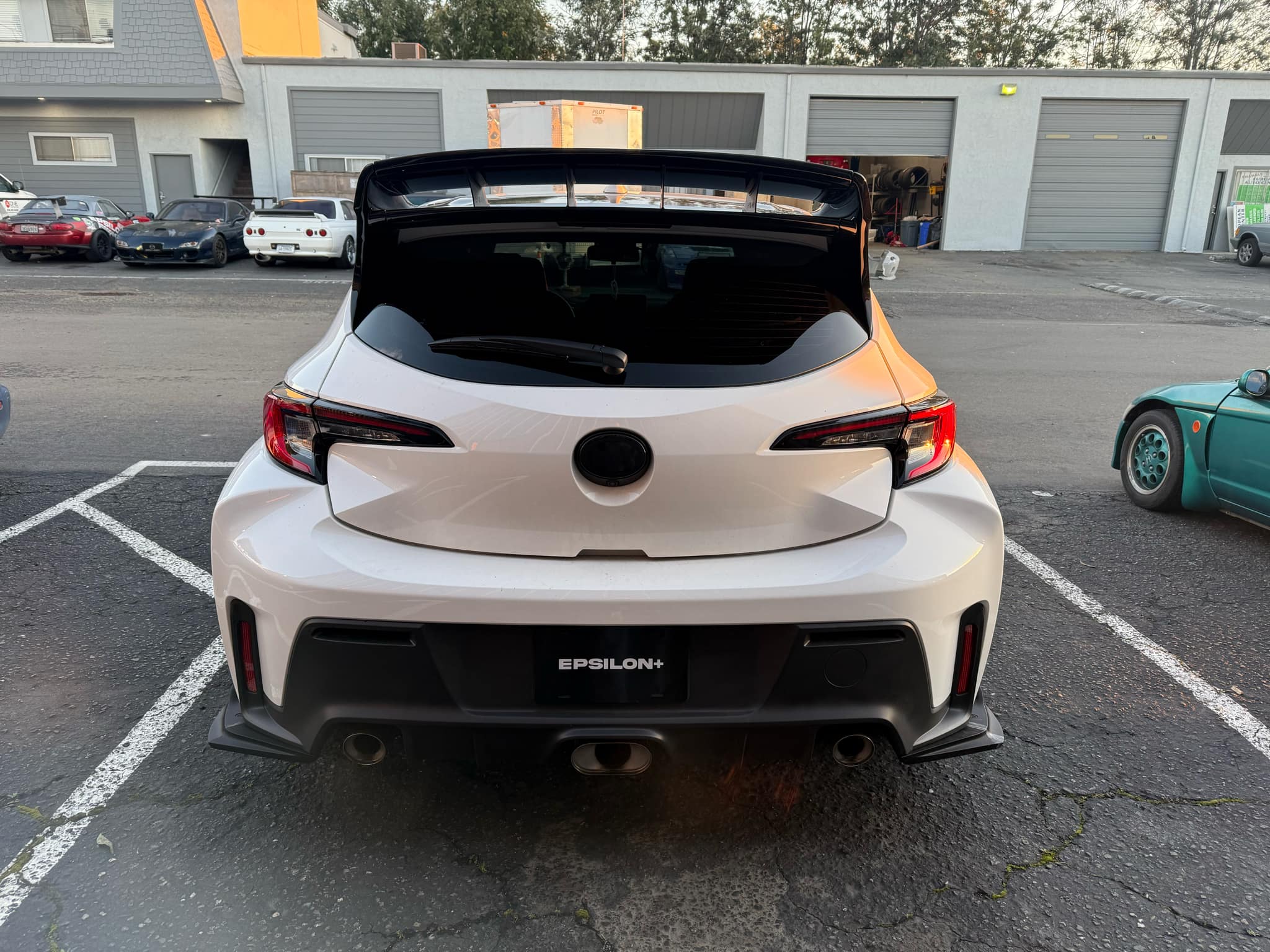 Rear view of a white GR Corolla with WRC Wing Strakes V2 parked next to other enthusiast cars