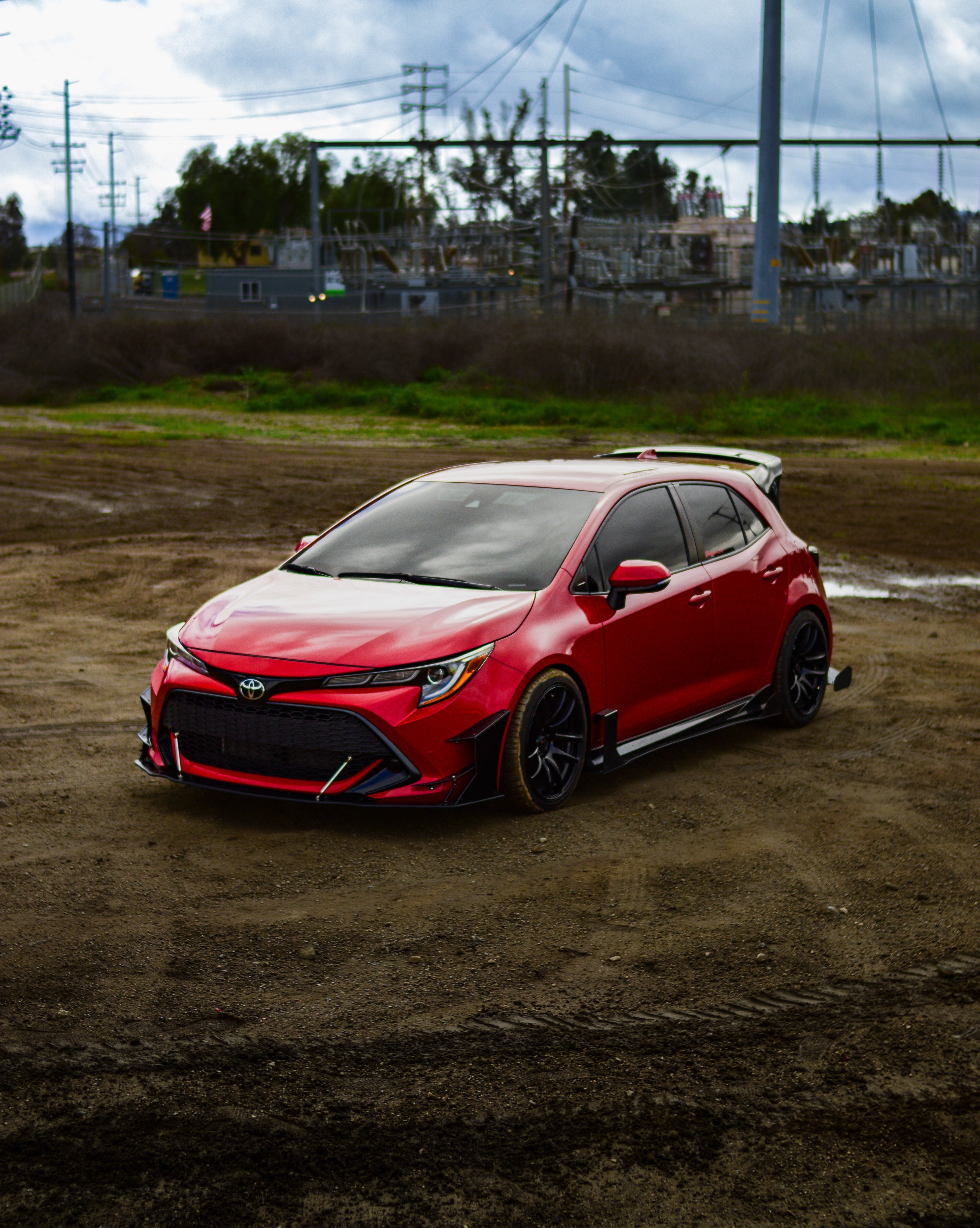 Front three-quarter view of a red GR Corolla with WRC Wing V3 on a dirt road
