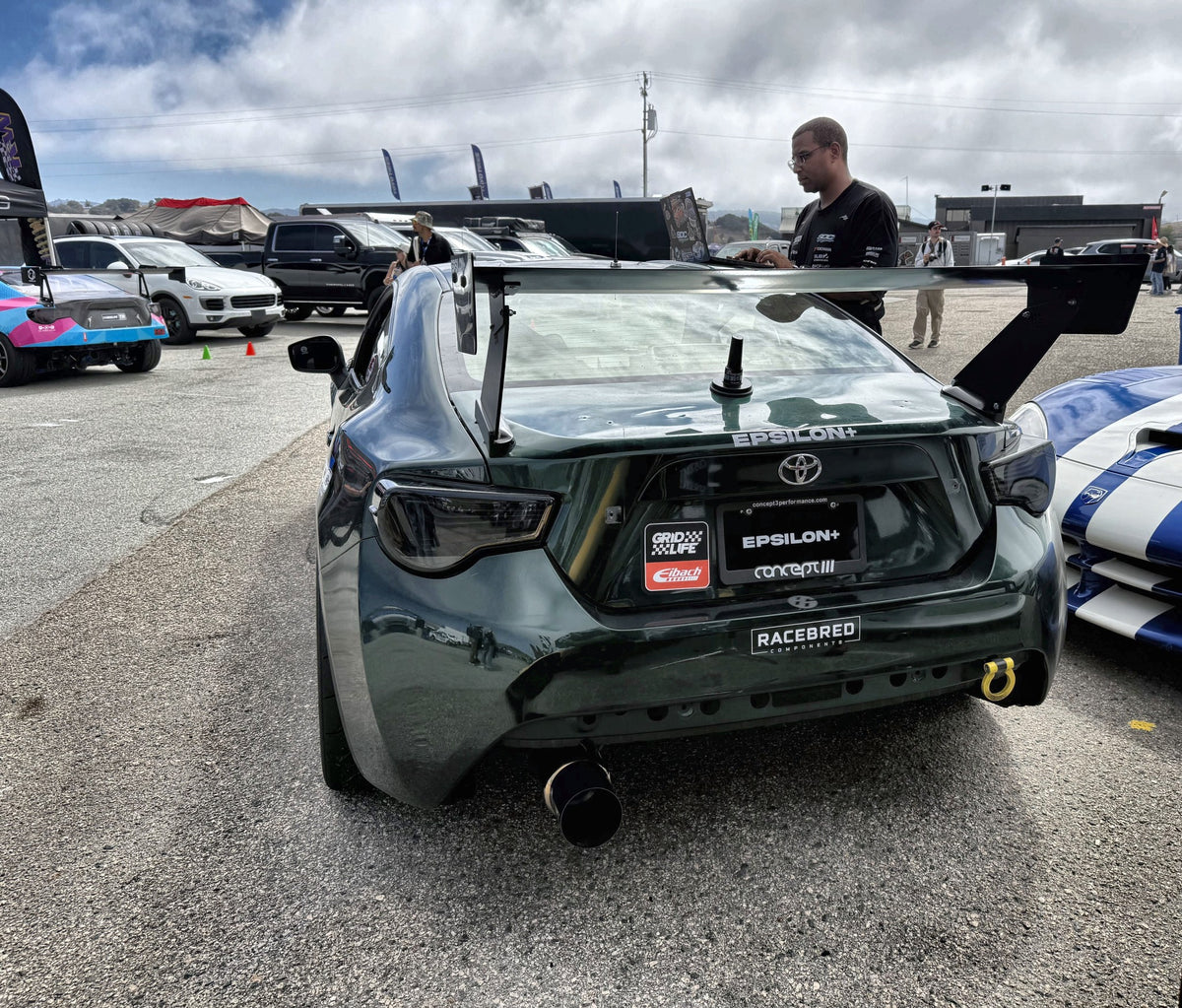 Rear view of a green Toyota GT86 (ZN6) race car with the Epsilon+ TC wing in a race paddock