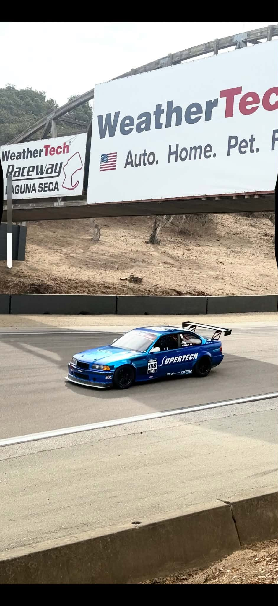 Blue BMW E36 race car with the Epsilon+ TC wing on track at WeatherTech Raceway Laguna Seca