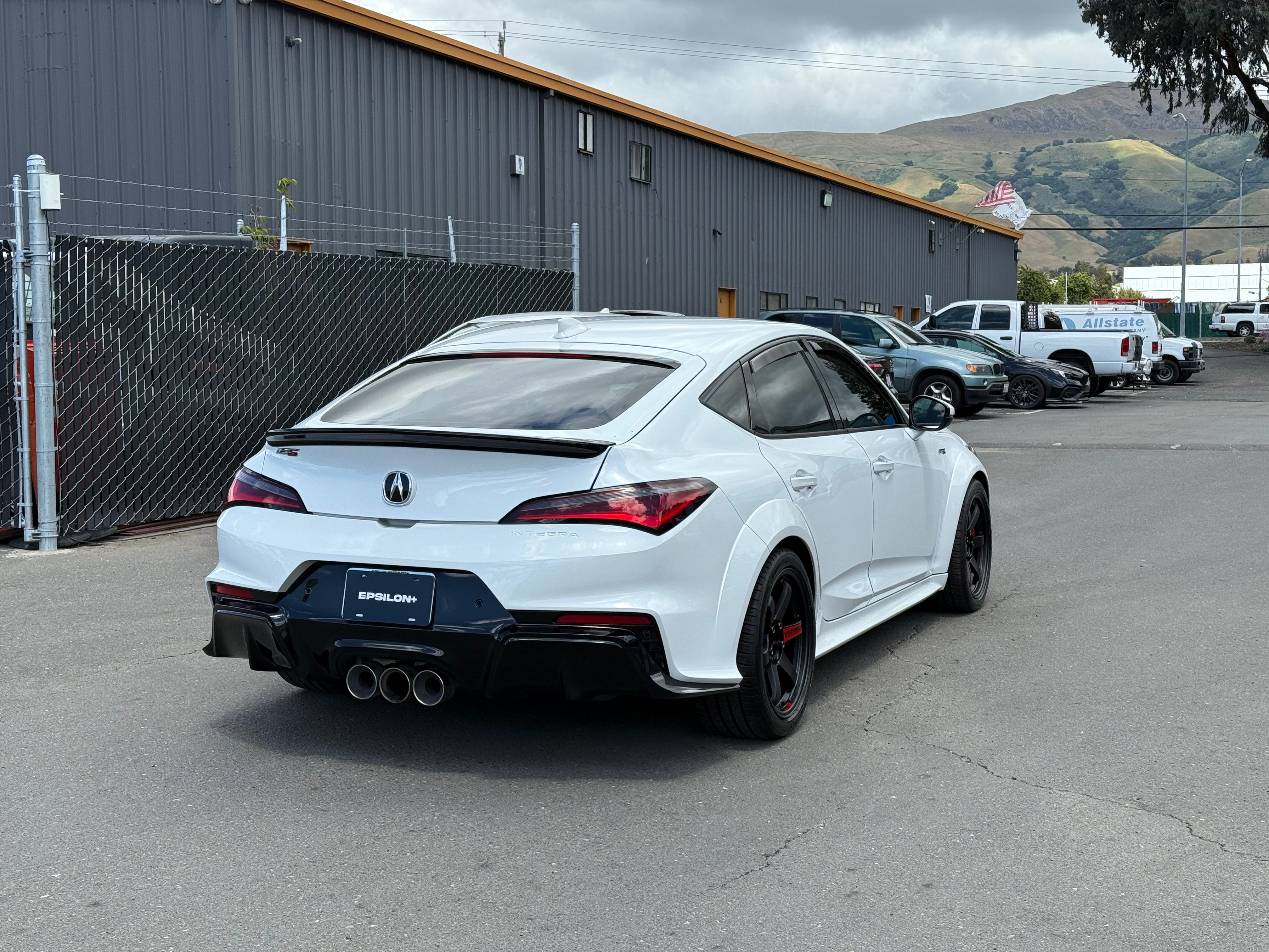 White Acura Integra with rear trunk lip parked beside a warehouse