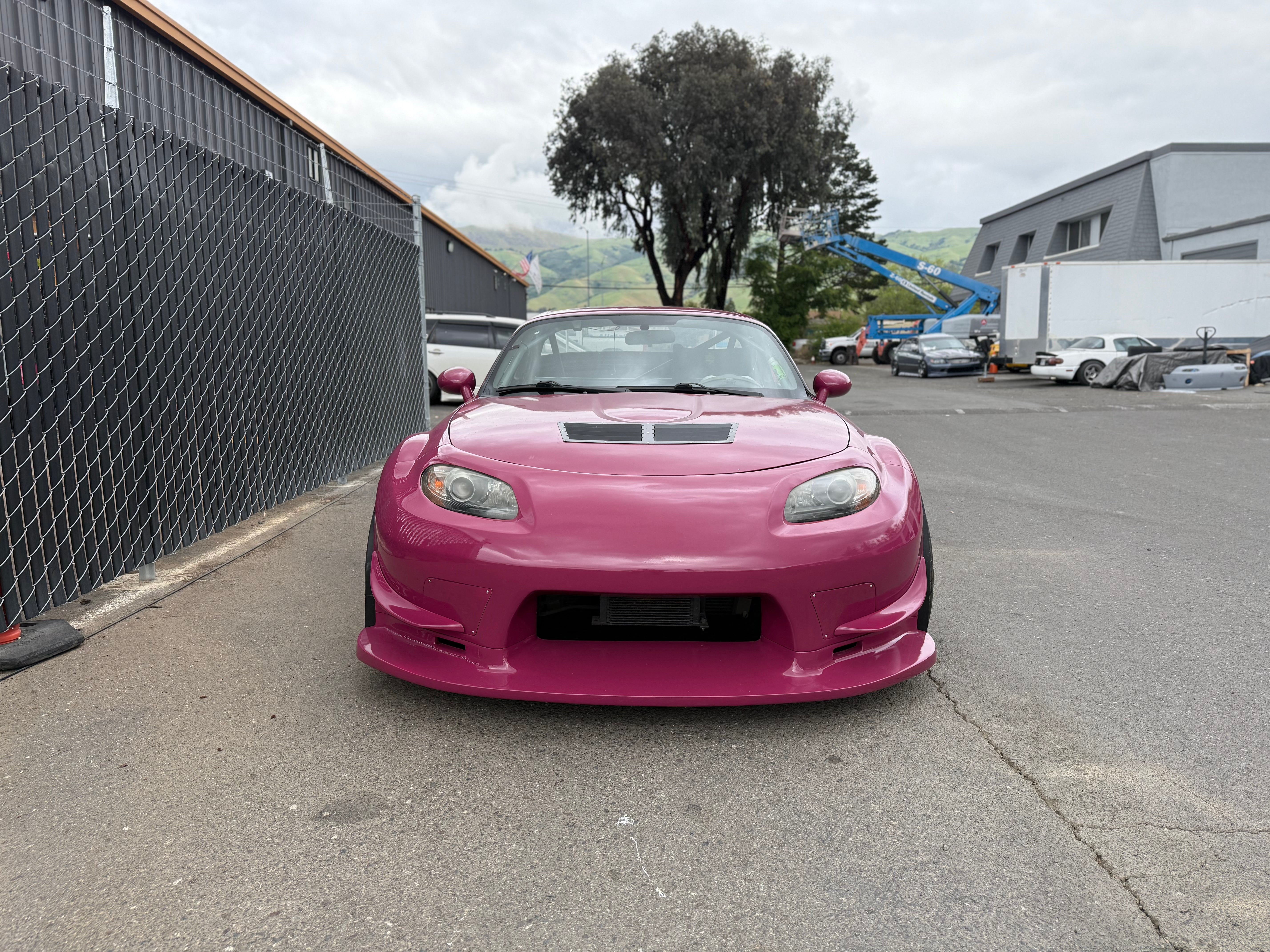 Pink Mazda MX-5 Miata NC with front bumper parked beside a fence