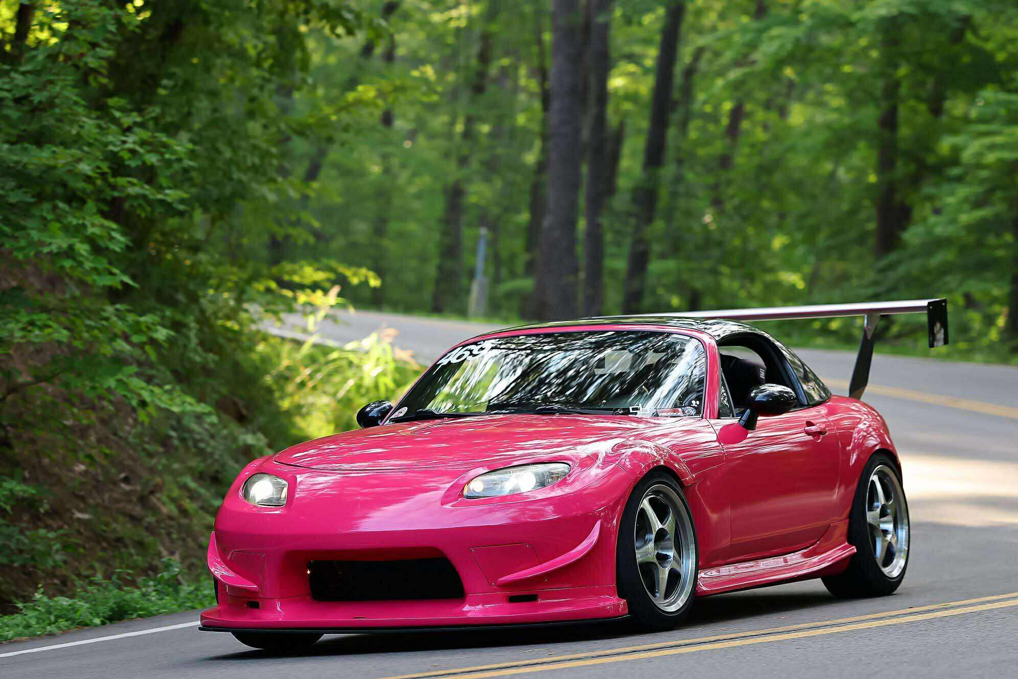 Pink Mazda MX-5 Miata NC with front bumper and rear wing on a wooded road