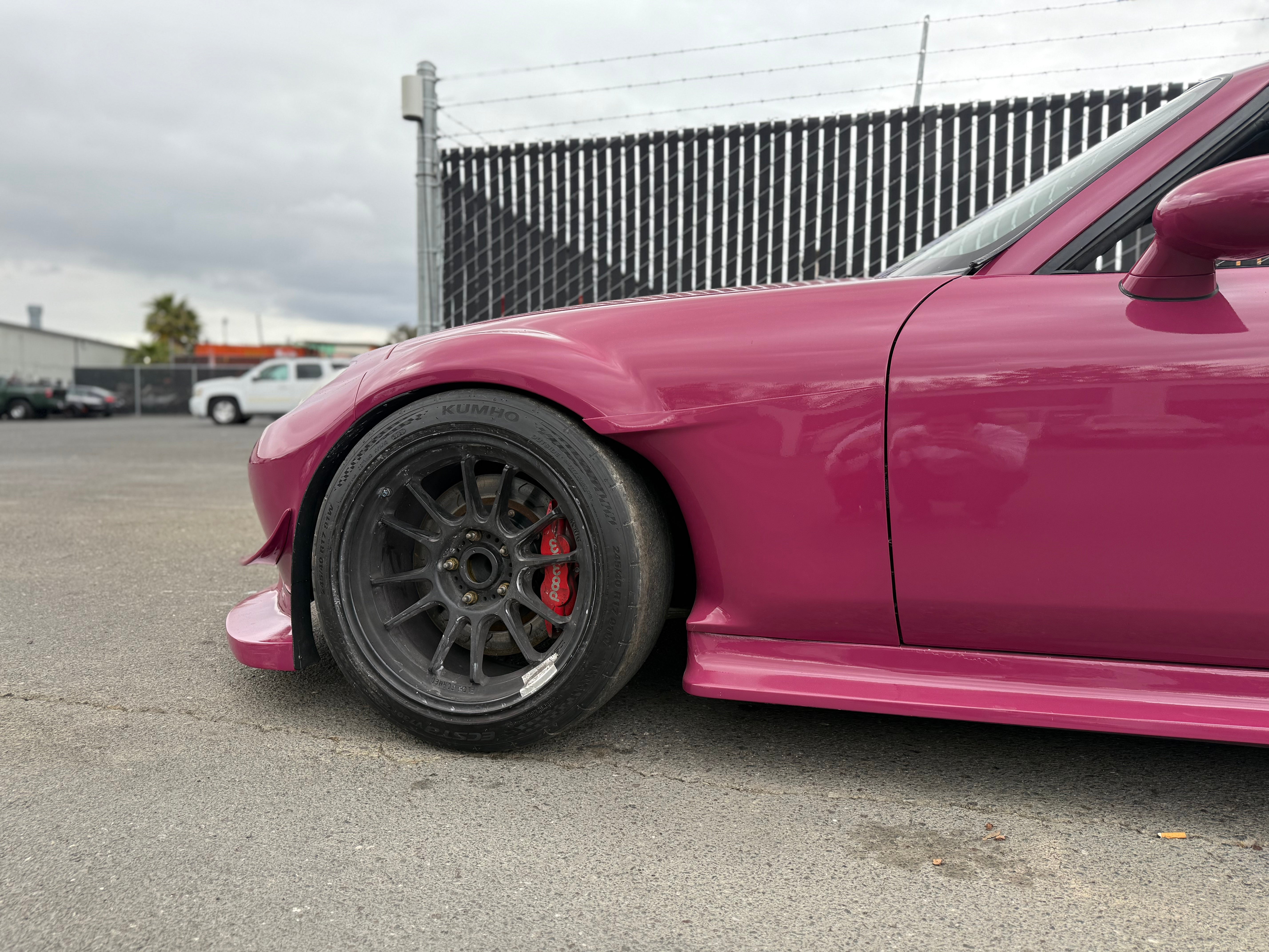 Low front three-quarter view of a pink Miata NC showing the side skirt and fender