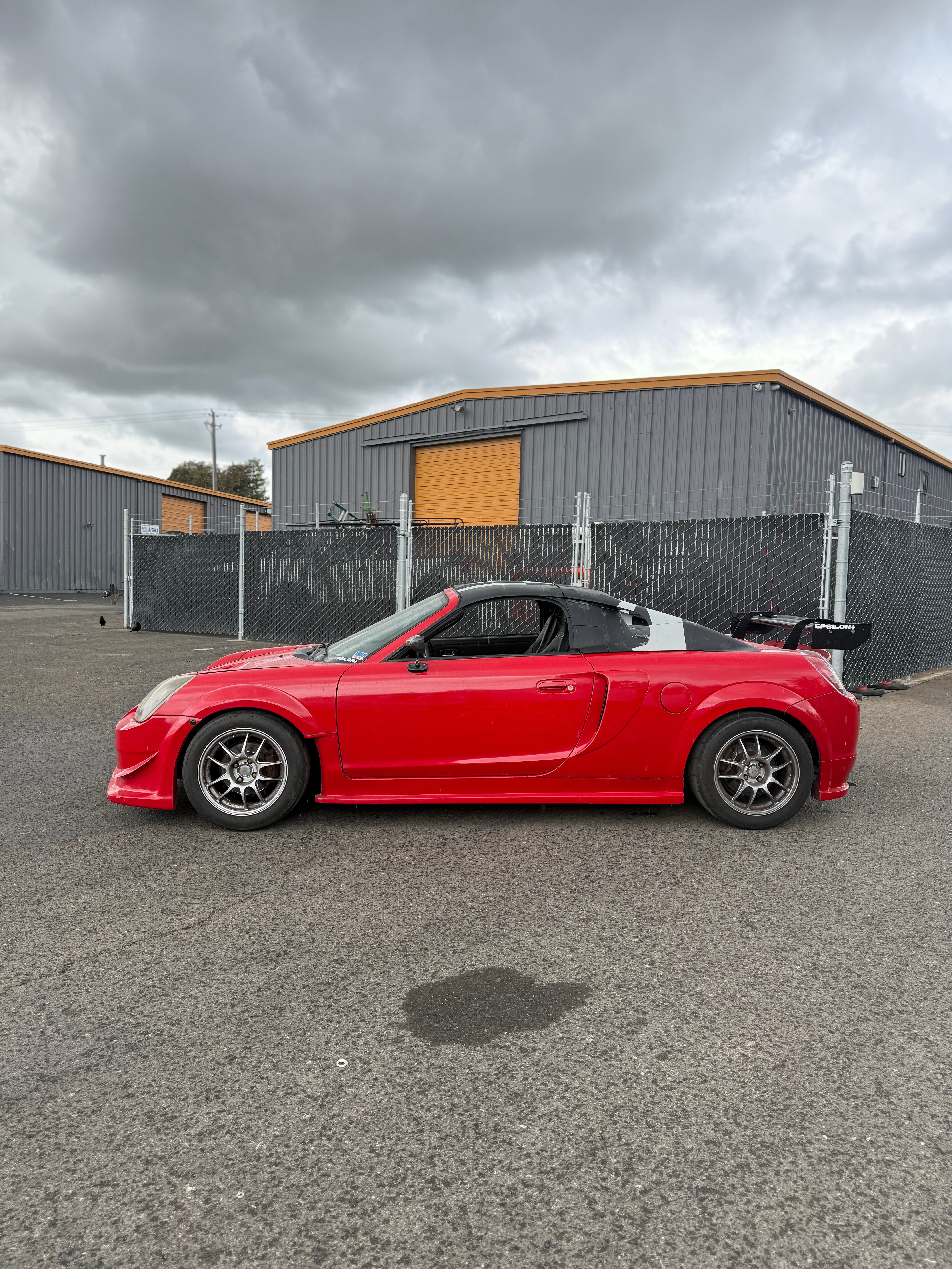 Side profile of a red Toyota MR2 Spyder under overcast skies