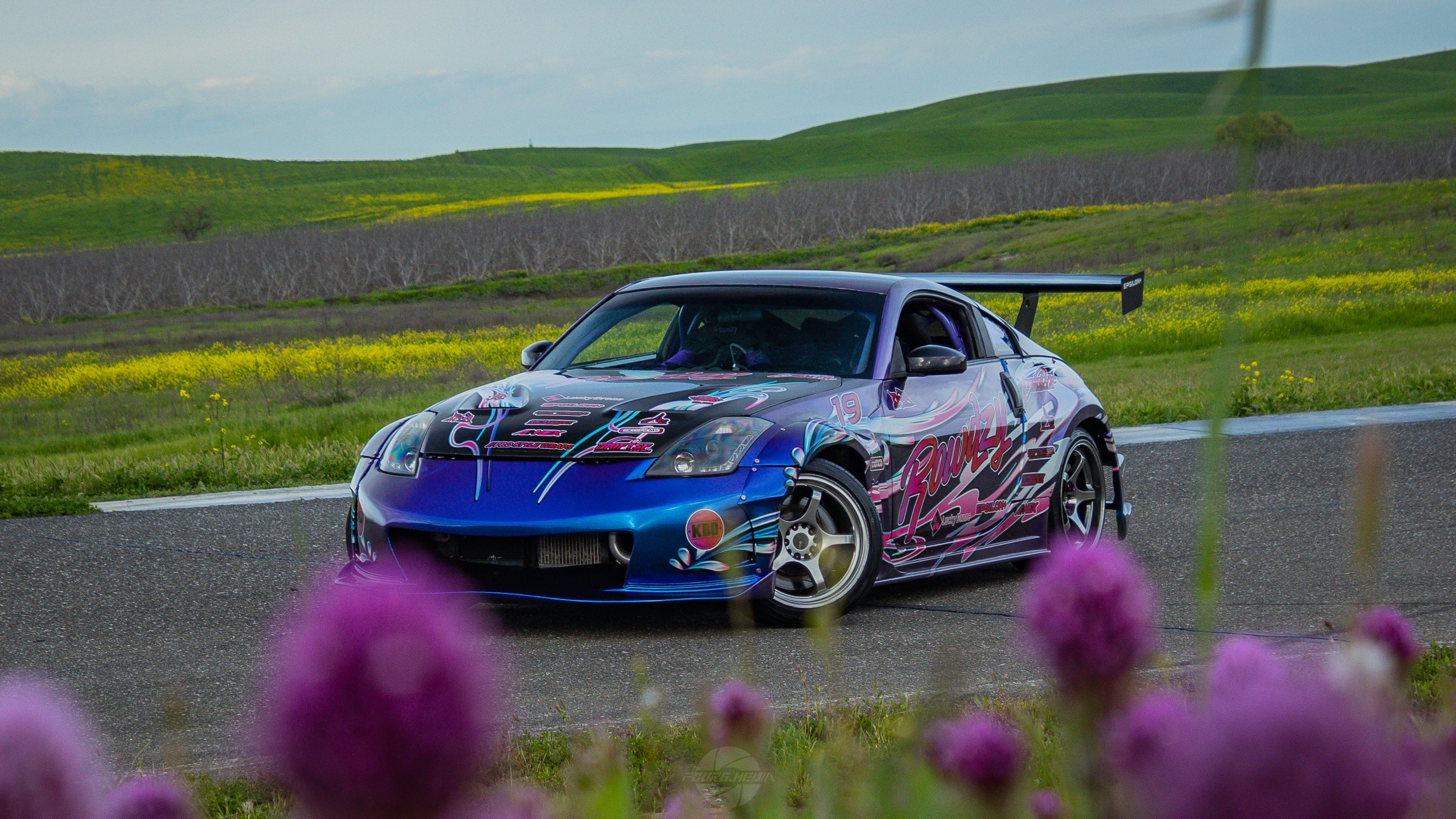 Front three-quarter view of a purple liveried Nissan 350Z with GT wing on a country road