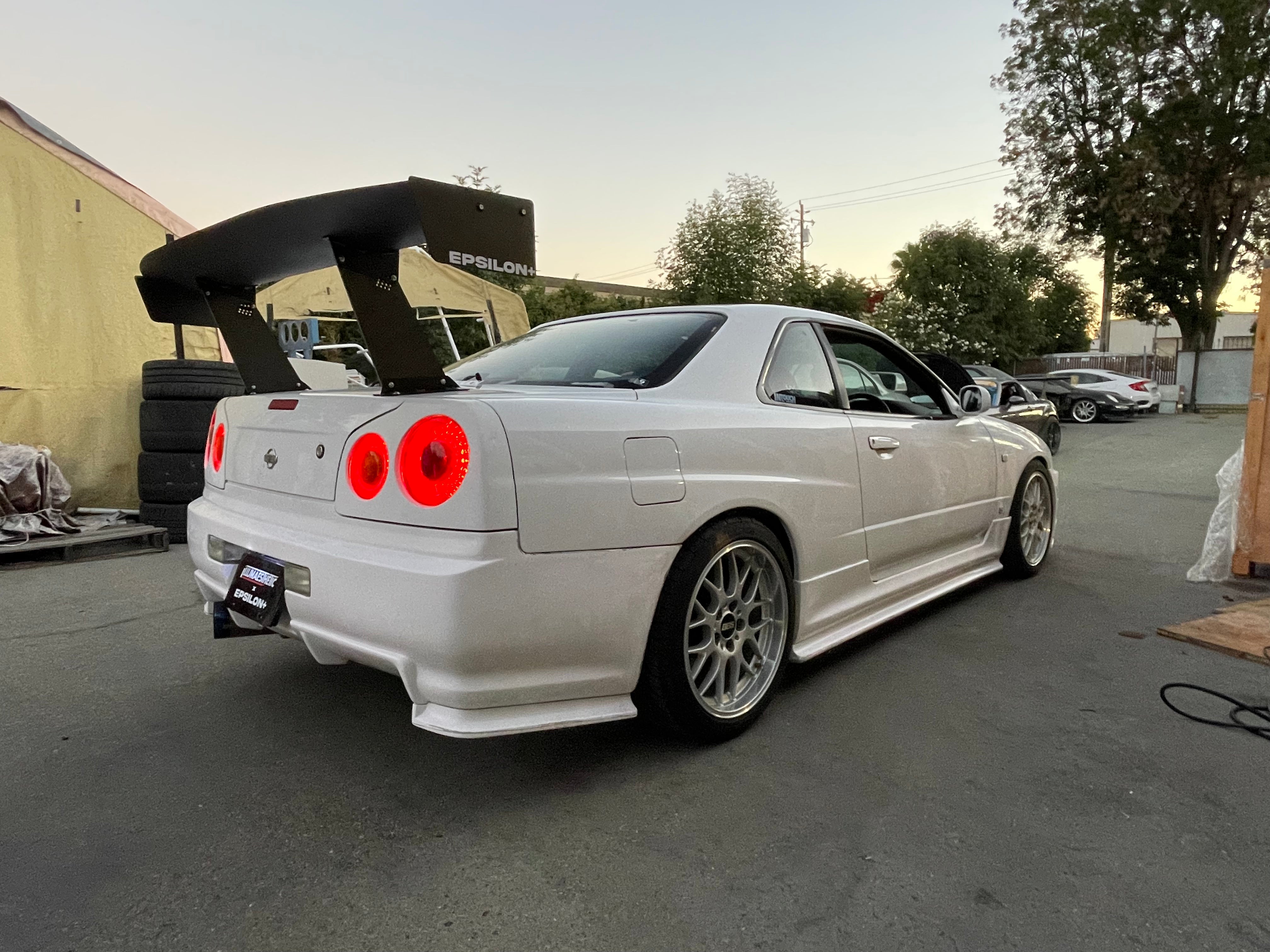 Rear three-quarter view of a white Nissan Skyline R34 with the Epsilon+ GT wing at sunset