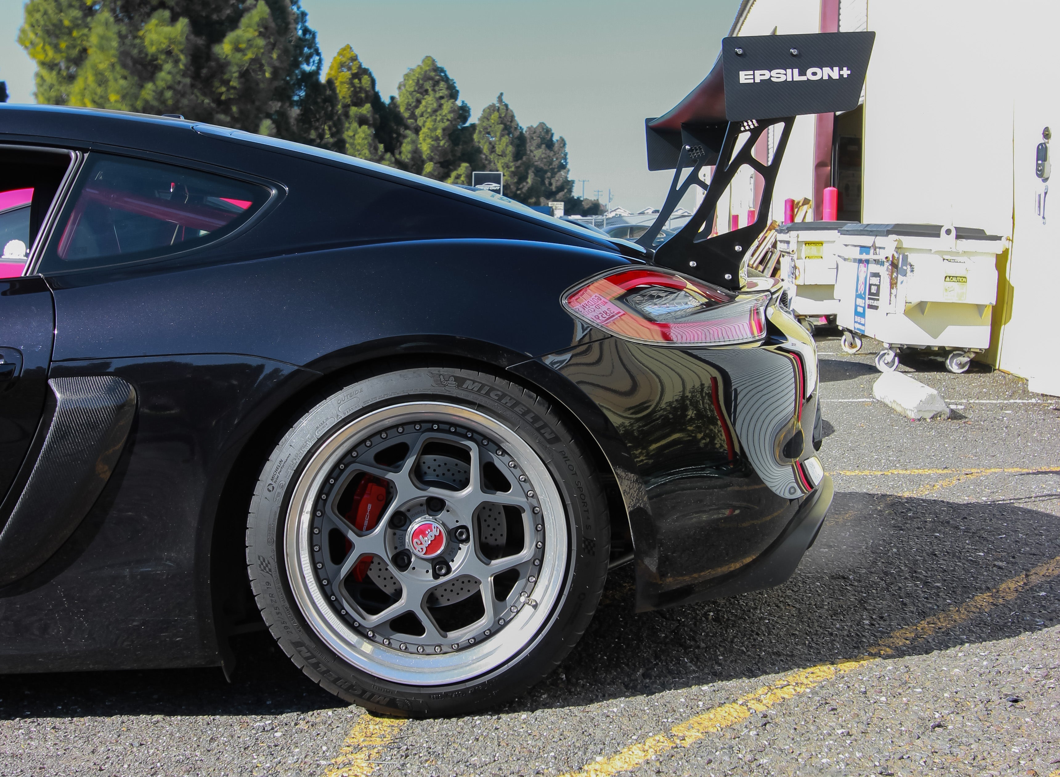 Close-up of a black Porsche Cayman rear wheel with GT wing visible above