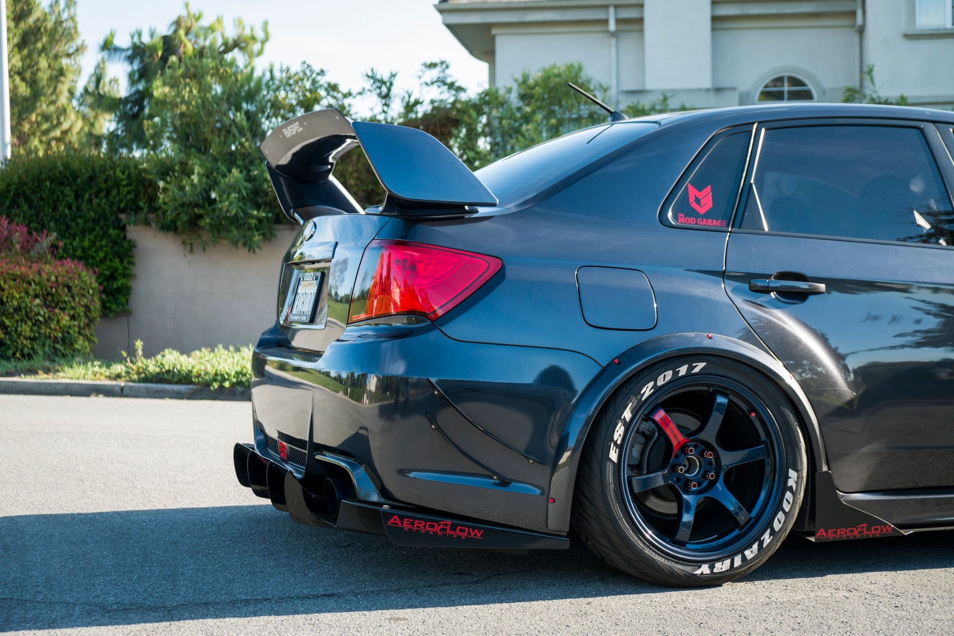 Rear three-quarter view of a gray STI Sedan with spoiler extension and bronze wheels