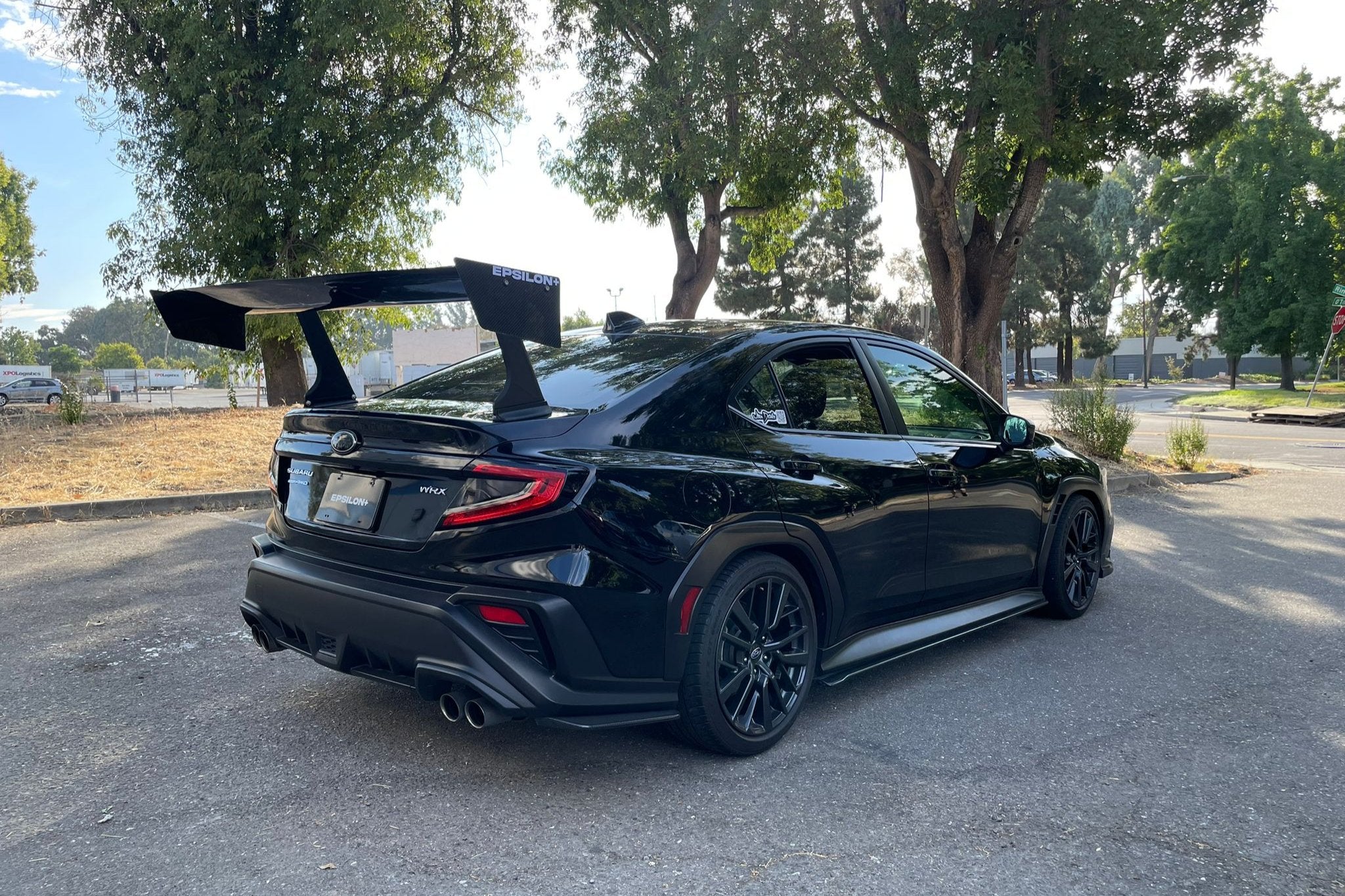 Black Subaru WRX VB with GT wing parked on a tree-lined street