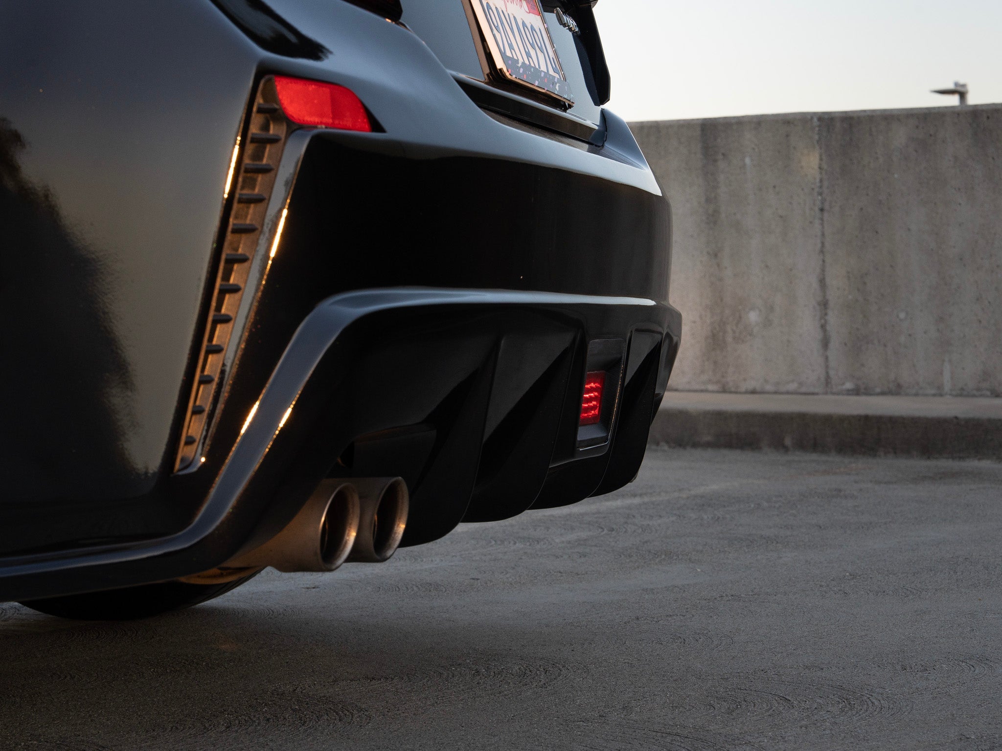 Rear view of a black Subaru WRX VB with rear bumper in a parking structure at dusk