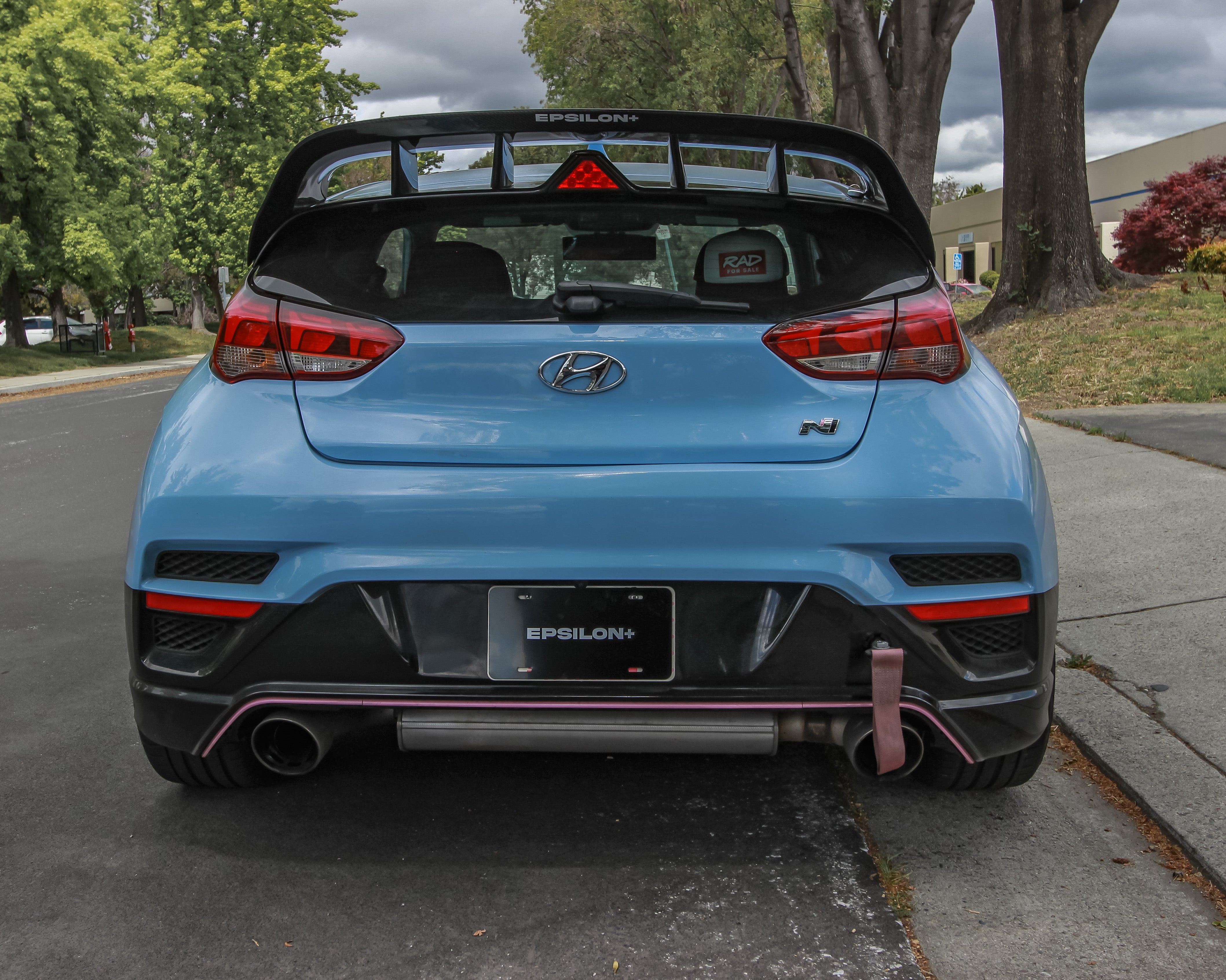 Rear three-quarter view of a red Veloster N with WRC Wing V2 on a wooded street