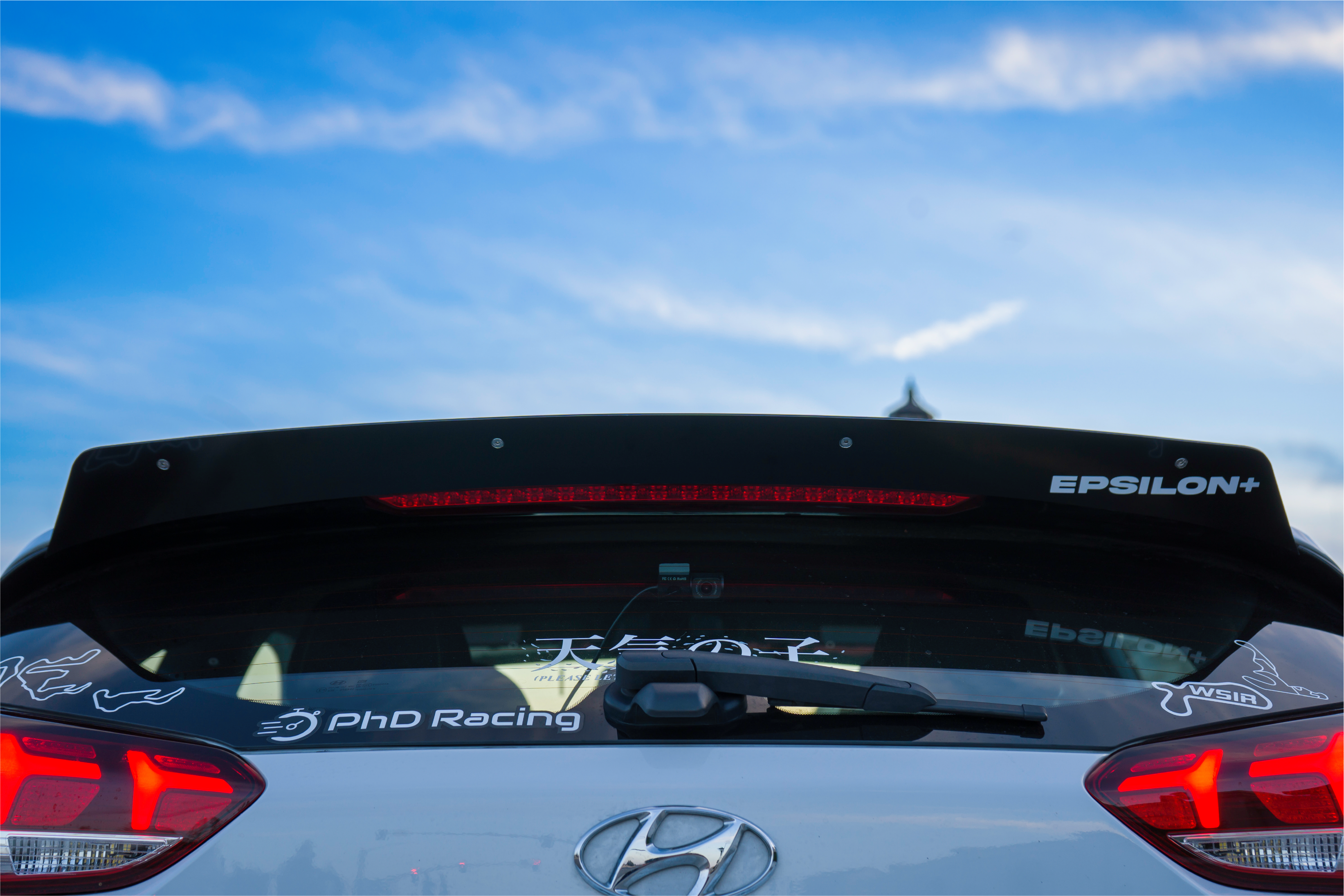 Rear three-quarter view of a white Veloster R with spoiler extension and racing decals