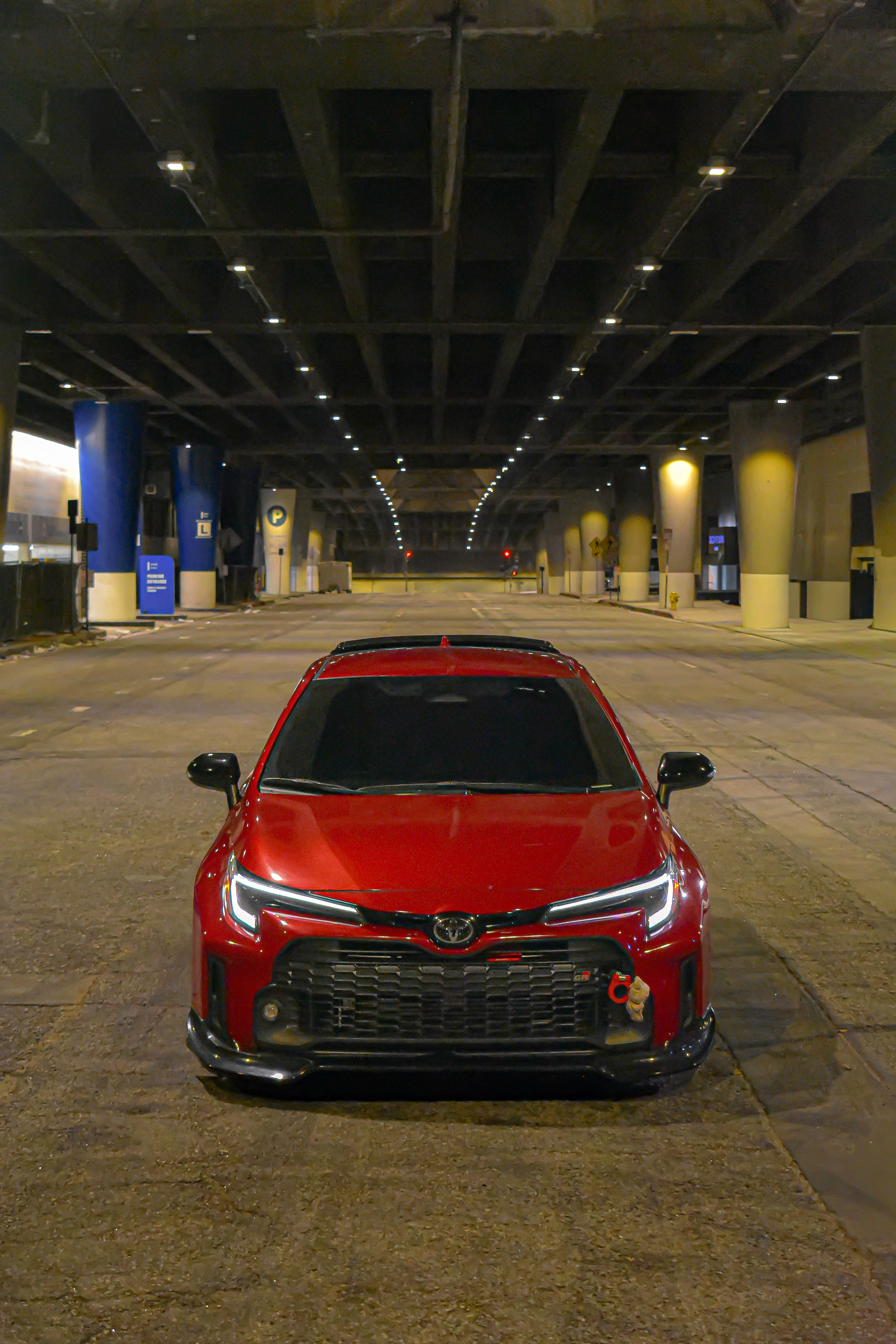 Front-on view of a red GR Corolla with front lip V2 parked in a parking garage at night