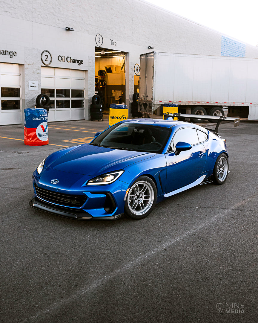 Front three-quarter view of a blue BRZ ZN8 with GT wing at an oil change shop