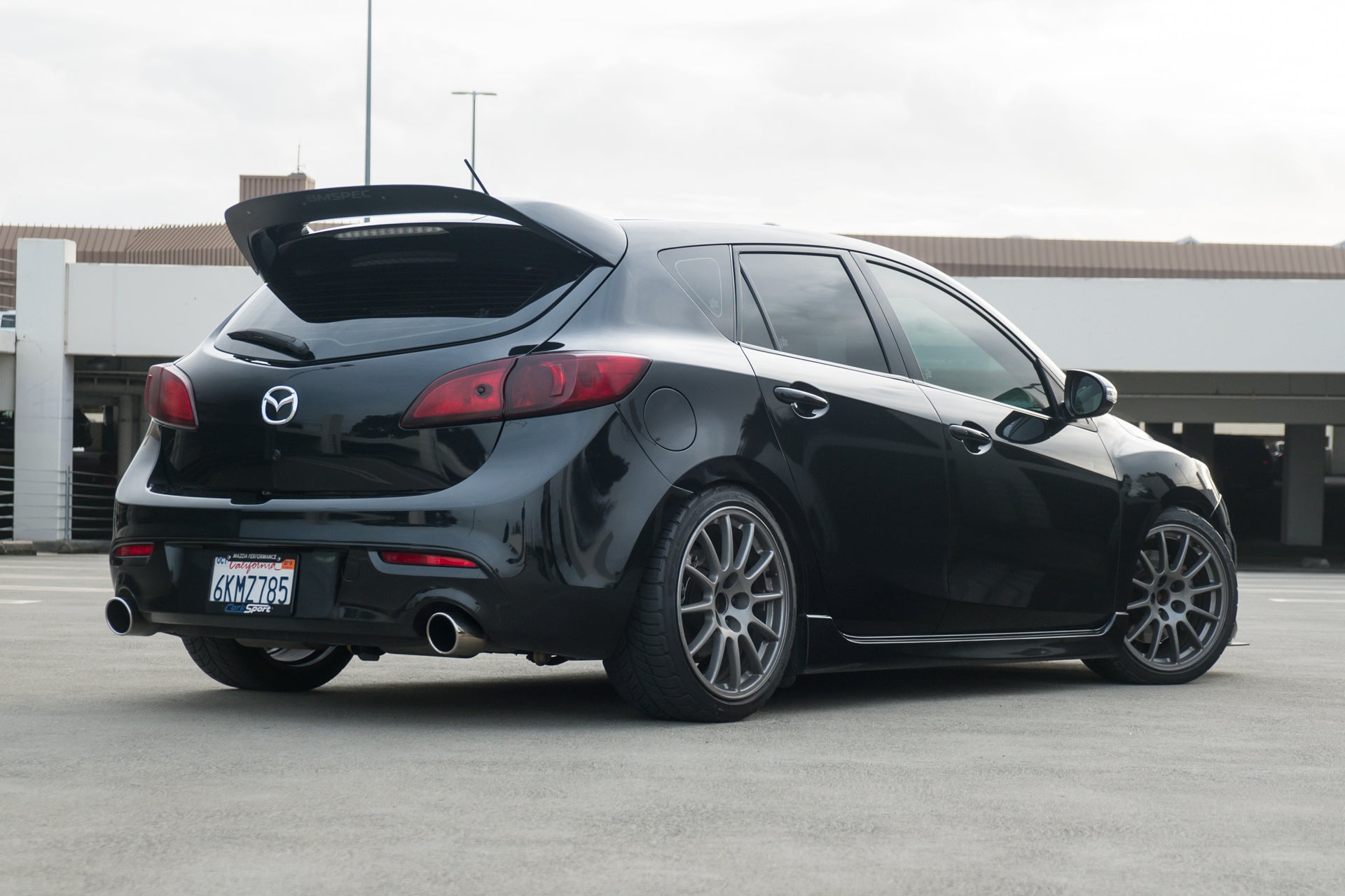 Rear view of a black Mazdaspeed3 Gen2 with spoiler extension in a parking garage