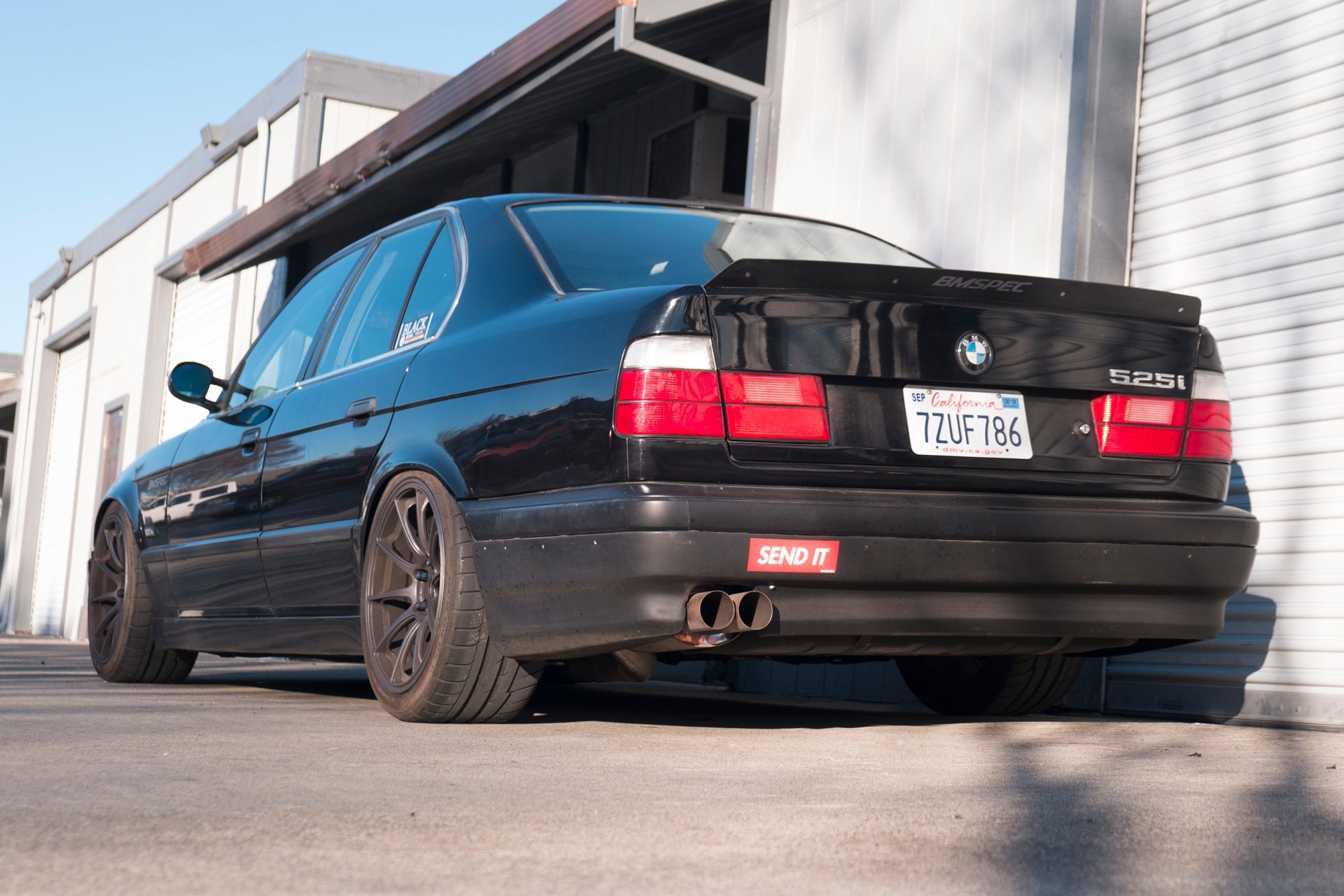 Rear three-quarter view of a black BMW E34 sedan with spoiler extension