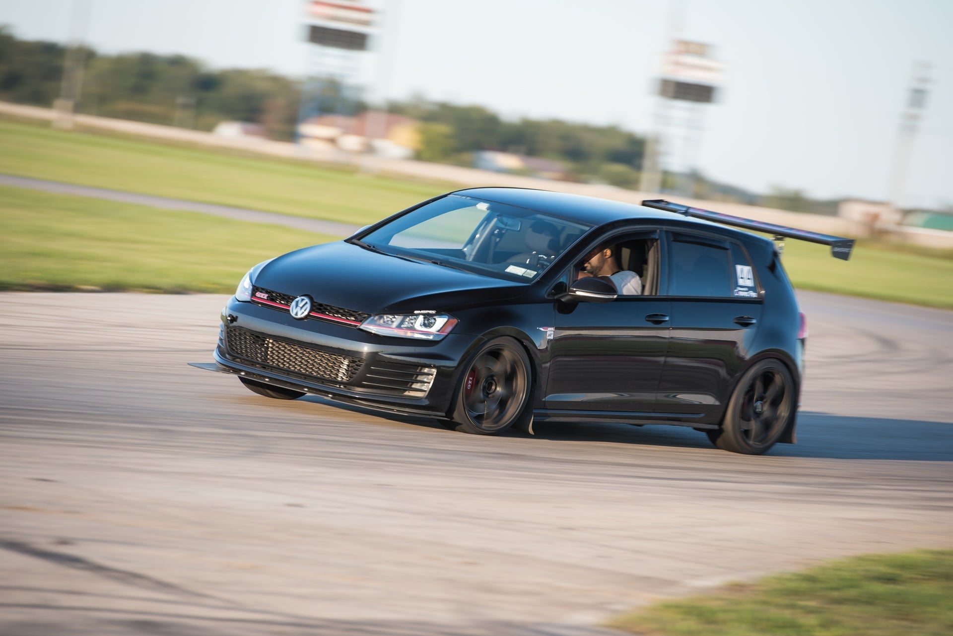 Black Golf GTI motorsport car with GT wing driving on a track