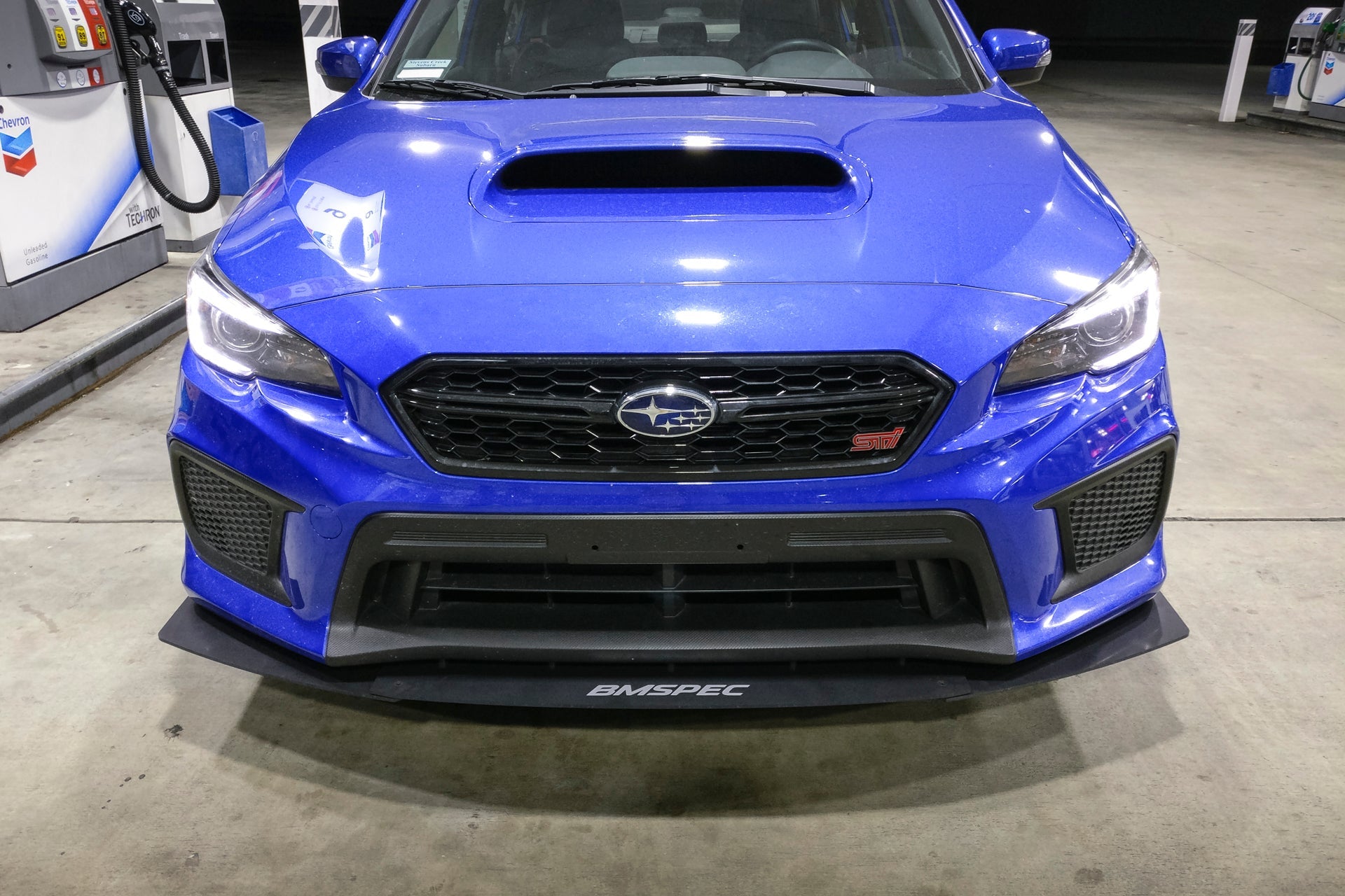 Front-on view of a blue Subaru WRX STI with front lip and headlights on