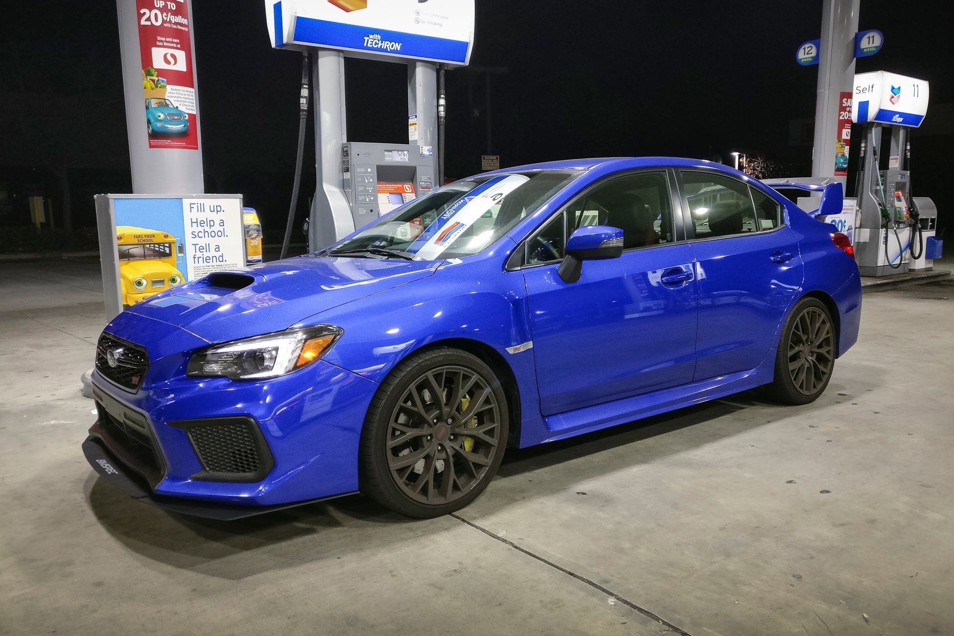 Front three-quarter view of a blue Subaru WRX STI with front lip at a gas station at night