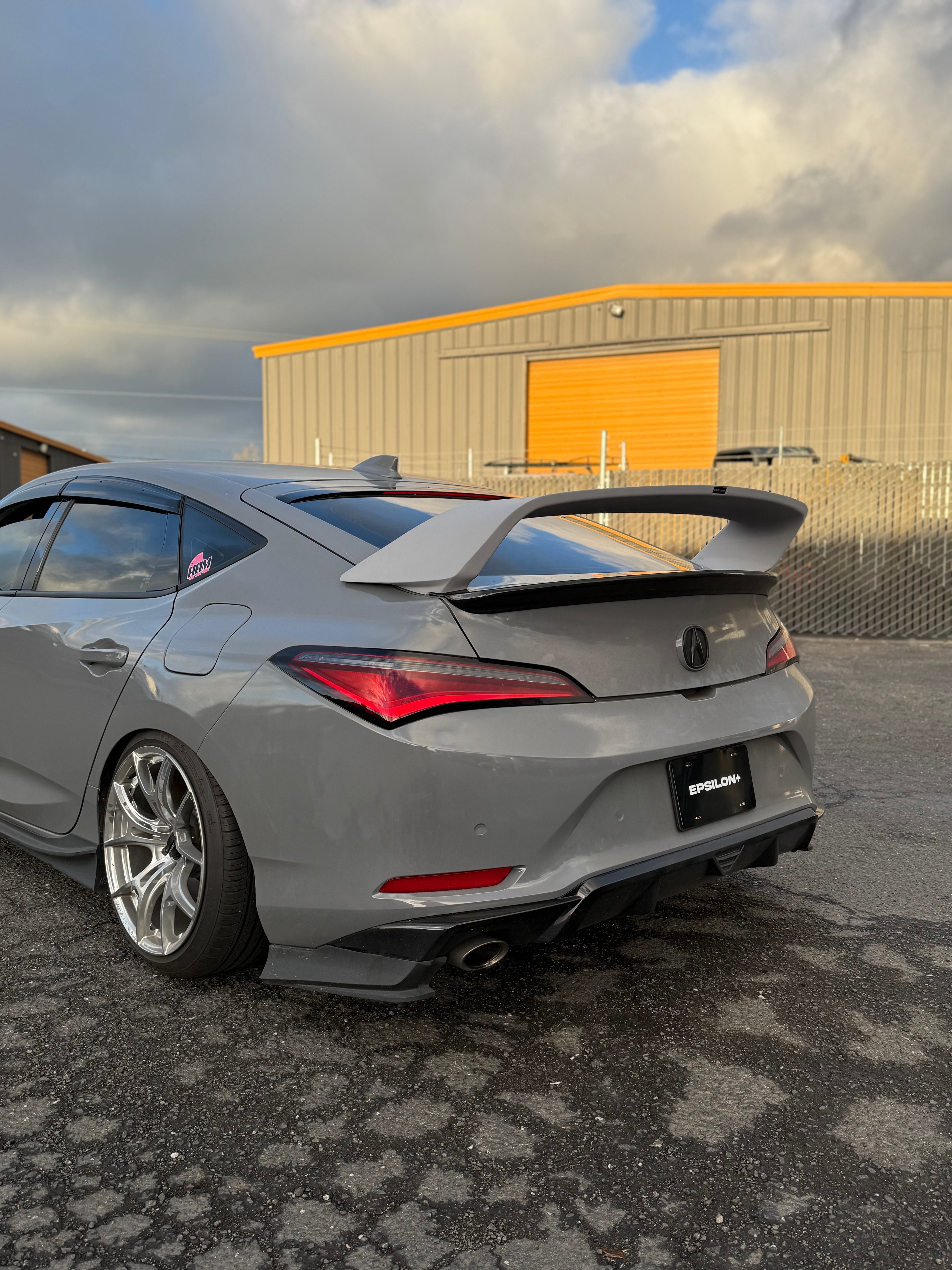 Rear three-quarter view of a silver Acura Integra with Sport Wing on cobblestone